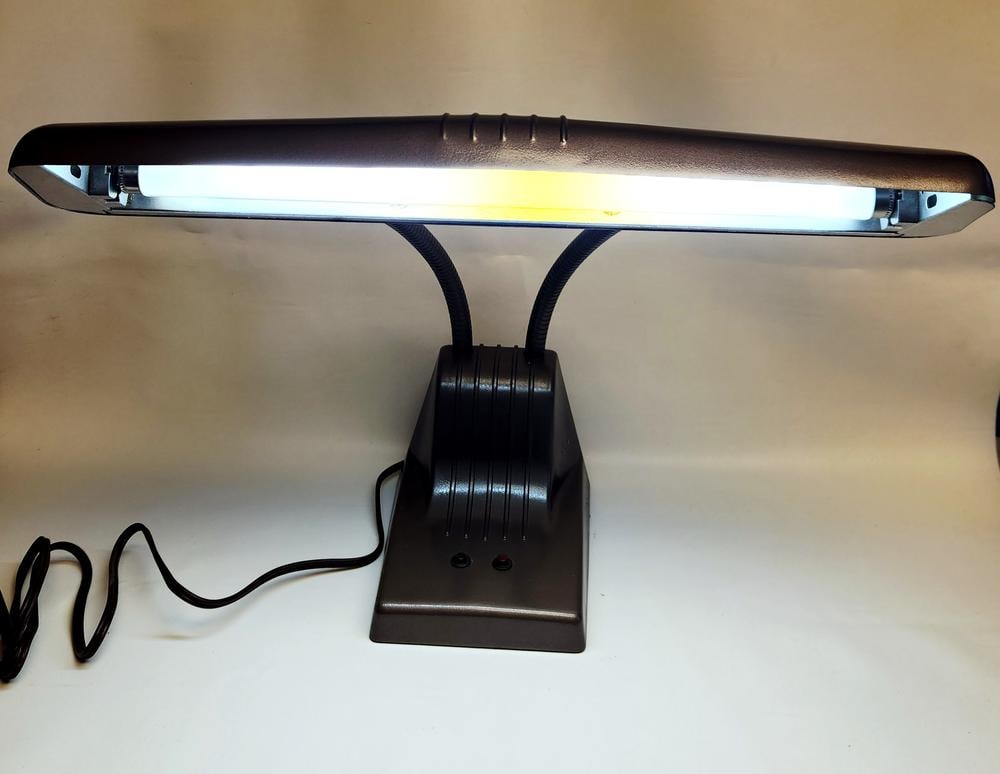 Industrial Style Bronze Finished Fluorescent Desk Lamp with Twin Gooseneck Arms: An industrial style fluorescent desk lamp featuring a textured metallic bronze finish. The lamp is designed with a wide, horizontal rectangular shade supported by two flexible gooseneck arms. The rect