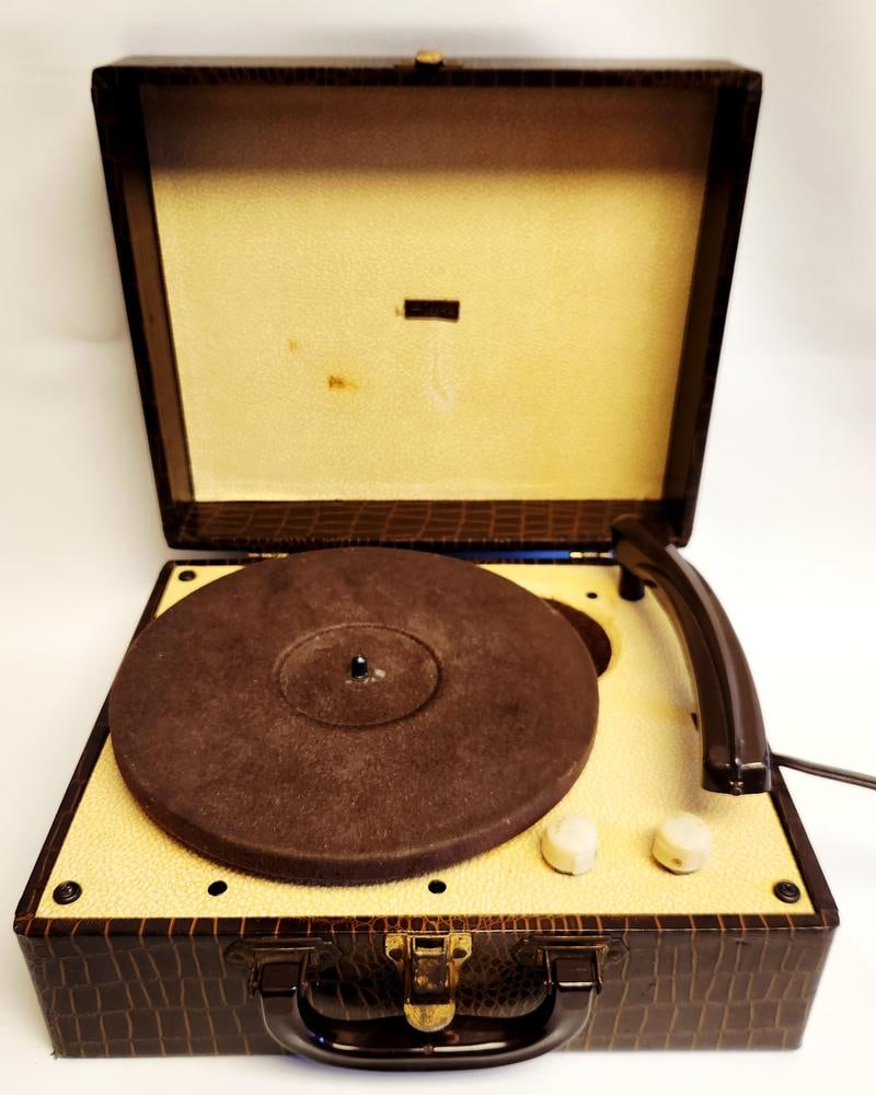Aldens Portable Record Player Faux Crocodile Case: This Aldens portable record player is housed in a brown faux crocodile-patterned carrying case featuring a dark plastic handle and brass-toned metal hardware. The interior is lined with a cream-colore