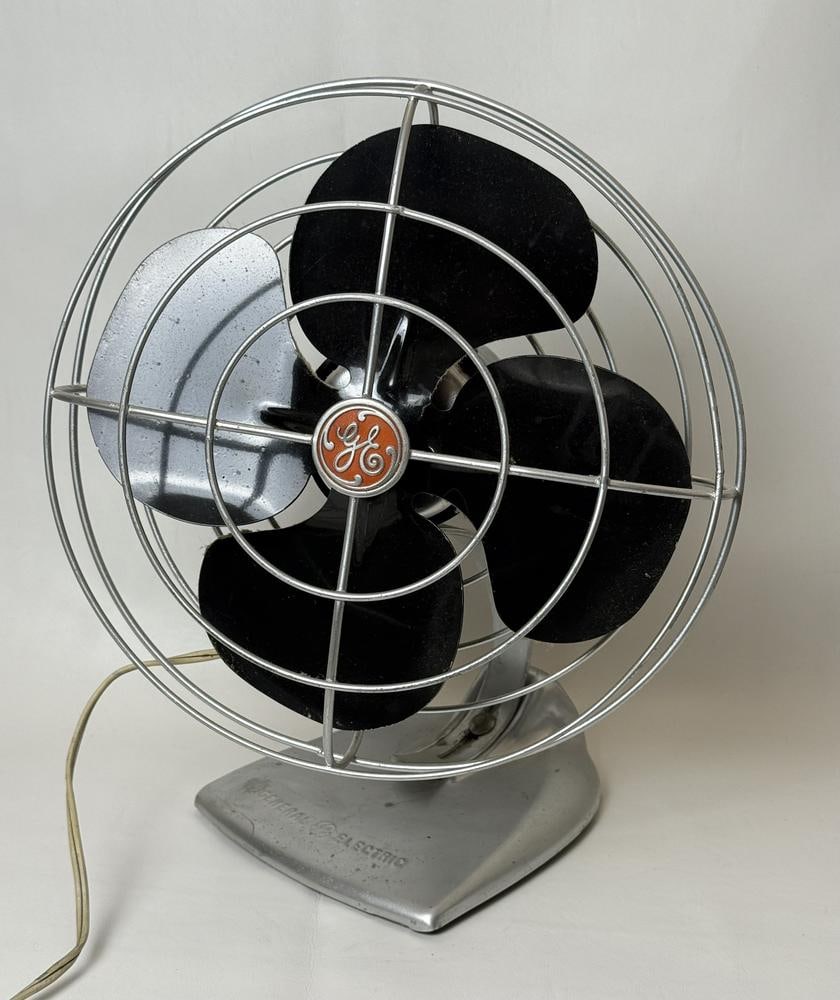 A General Electric Oscillating Metal Desk Fan: This item is located on the second floor. A General Electric oscillating metal desk fan featuring a mid-century modern design. The fan is constructed with a silver-toned metal base and wire cage, hous
