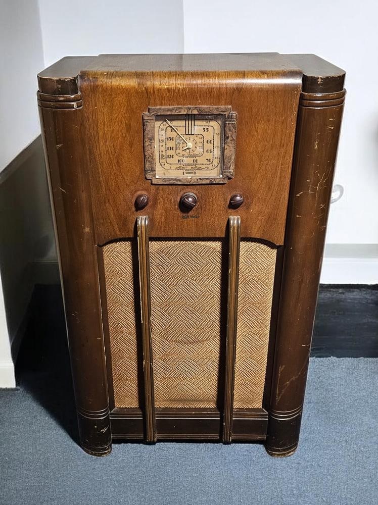 RCA Victor Art Deco Console Radio: Measures 40 x 24 x 12 inches. The wooden cabinet exhibits age-consistent wear including surface scratches, scuffs to the finish, and a veneer separation on the upper left side. Powers on,