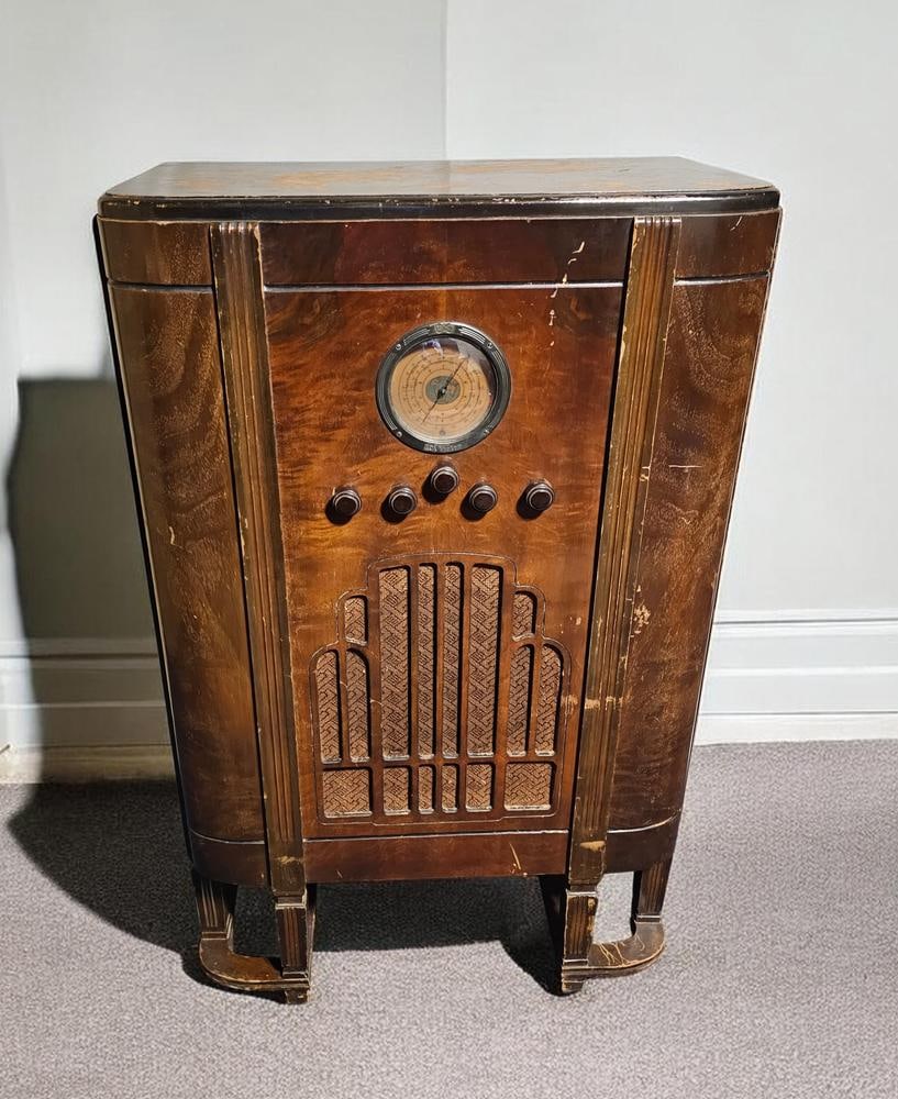 RCA Victor Model 224 Art Deco Floor Console Radio: This RCA Victor Model 224 floor console radio features a wood-veneered cabinet in the Art Deco style with a rounded front and stepped base. The central control panel consists of a circular dial with a