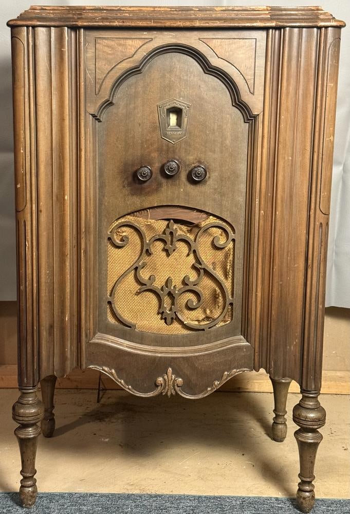 Kennedy Model 32 Console Radio: This item is located in the basement. A Kennedy Model 32 console radio featuring a wooden cabinet with Art Deco and Gothic Revival stylistic influences. The cabinet is designed with fluted side pilast