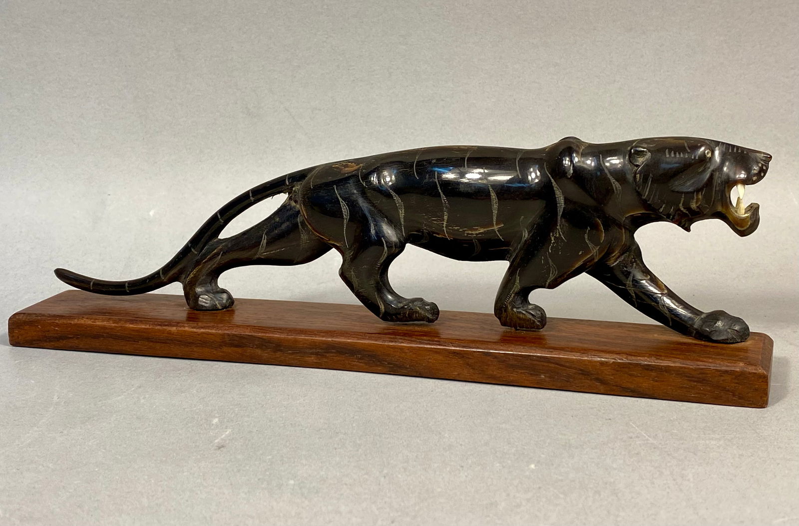 A Carved Horn Figurine of a Stalking Tiger on Wooden Base: A carved horn figurine depicting a stalking tiger, mounted on a rectangular wooden base. The figure is constructed from polished dark water buffalo horn and features hand-etched stripes along the