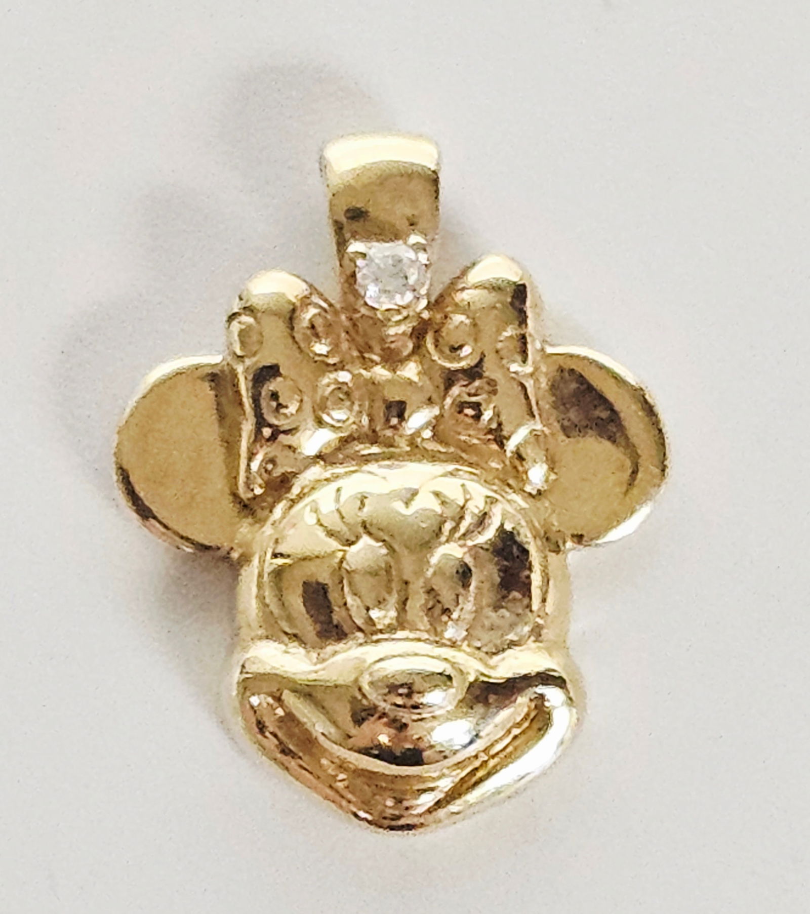 14K Gold Disney Minnie Mouse Pendant 3.1 Grams: A 14K yellow gold pendant designed in the form of Disney character Minnie Mouse. The piece features a polished front depicting the character wearing a bow and a textured reverse. A single small, round