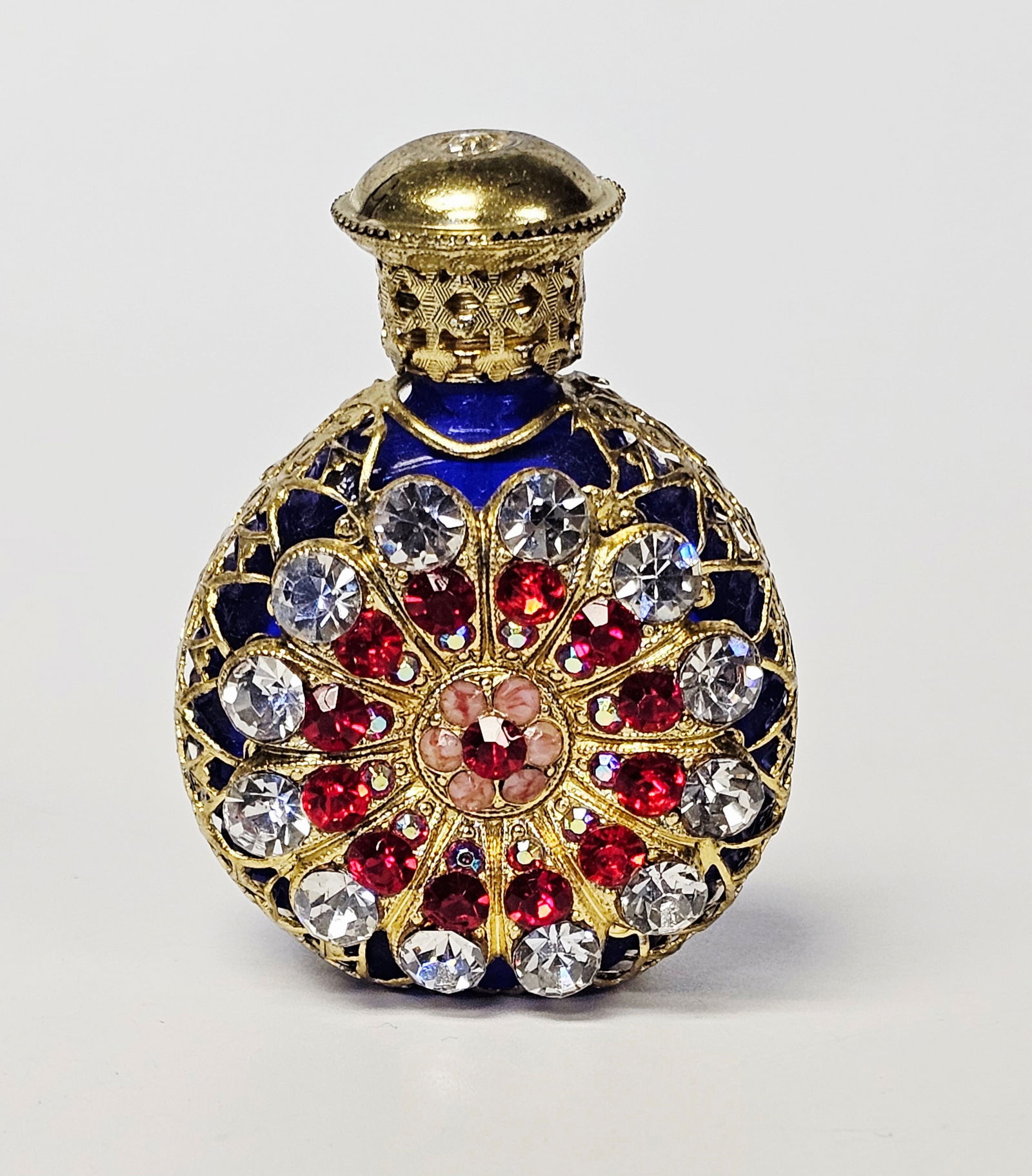 Vintage Czech Cobalt Glass and Filigree Perfume Bottle: A vintage Czech glass perfume bottle featuring a cobalt blue glass body encased in a gold-tone metal filigree overlay. The front of the bottle displays a radial floral motif embellished with faceted