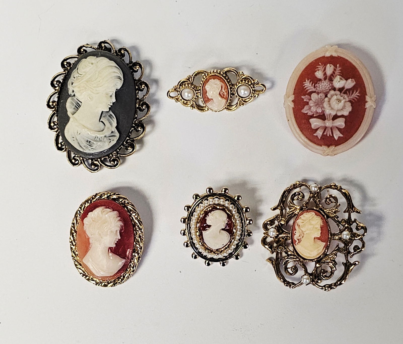 Vintage Victorian Style Costume Jewelry Cameo Brooches: A collection of vintage Victorian style costume jewelry cameo brooches featuring molded resin or plastic cameos set in gold-tone base metal frames. The group includes several pieces depicting classica