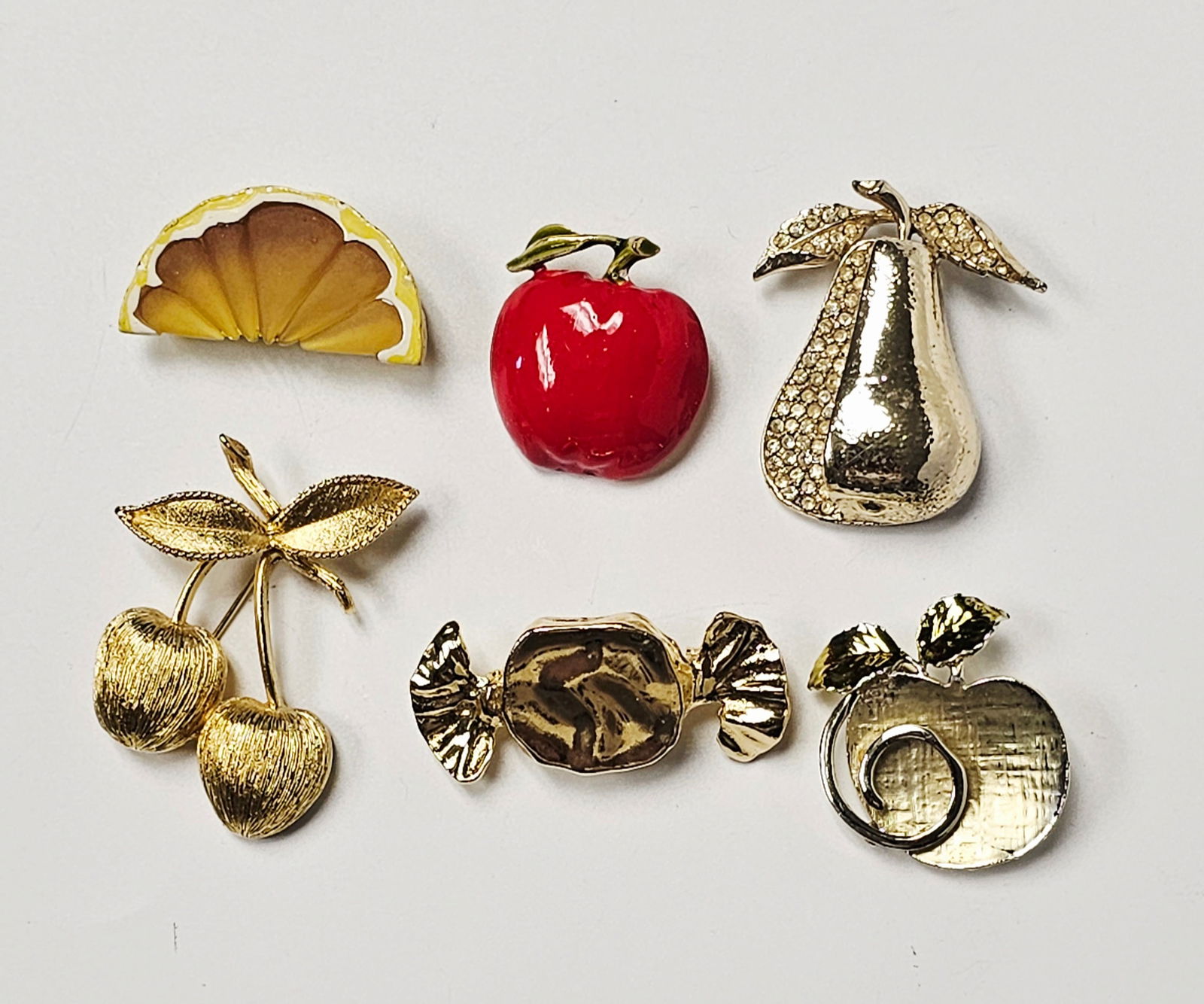 Vintage Costume Jewelry Brooches Inc Sarah Coventry: This collection of vintage costume jewelry features a variety of novelty brooches in fruit and confectionery motifs. The group includes a gold-tone pear-shaped brooch accented with clear