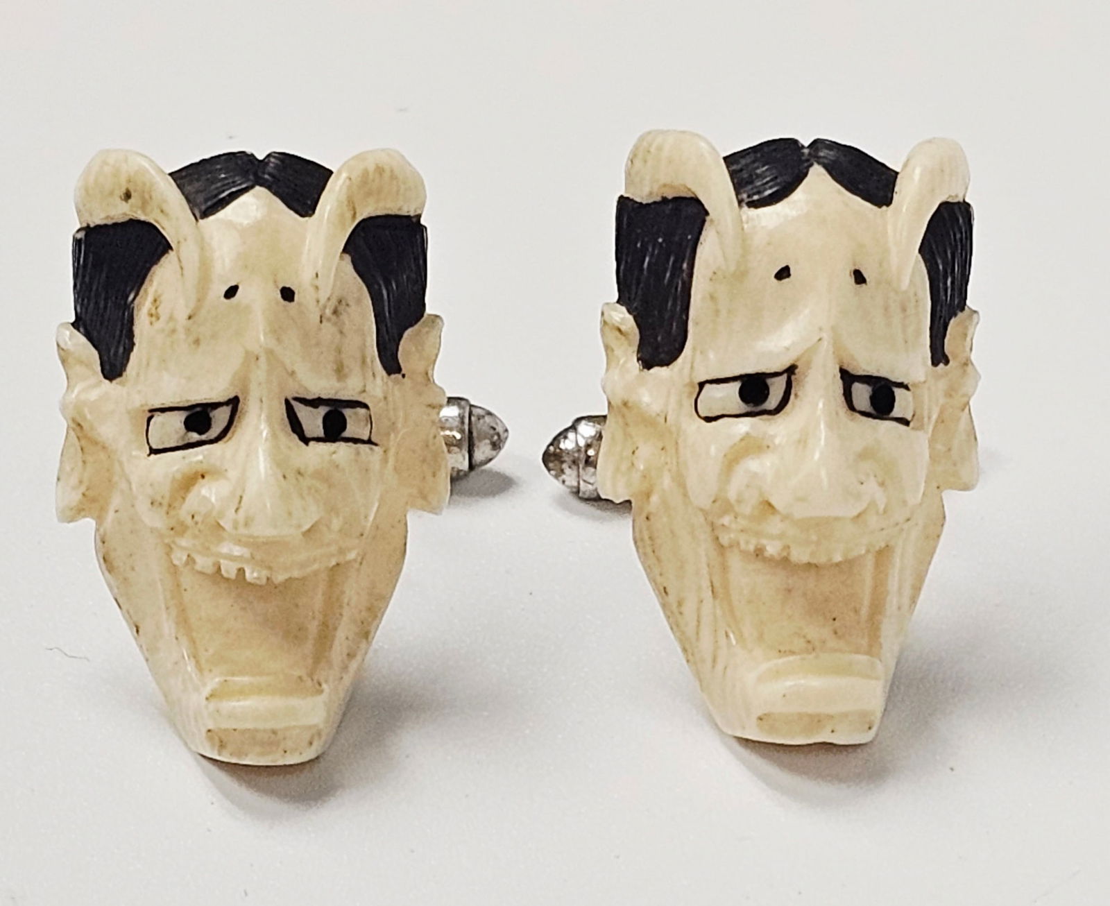 Vintage Carved Japanese Hannya Mask Cufflinks: A pair of vintage cufflinks featuring hand-carved masks in the style of Japanese Noh theater, specifically depicting the Hannya demonic figure. The masks are fashioned from an off-white material,