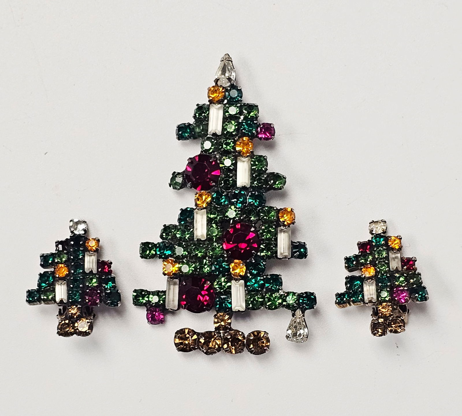 A Trio of Weiss Rhinestone Christmas Tree Jewelry: A trio of mid-century festive jewelry by Weiss, comprising a Christmas tree-themed brooch and a pair of matching clip-on earrings. Each piece is constructed in a tiered evergreen form, set with