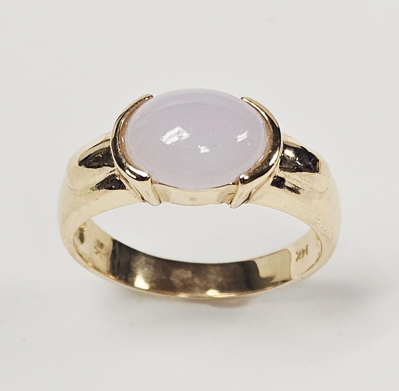 14K Gold and Lavender Cabochon Ring 3.3 Grams: A 14K yellow gold ring featuring a centrally set oval cabochon gemstone in a pale lavender hue. The gemstone is held in an integrated setting within a wide, tapered band designed with split shoulders