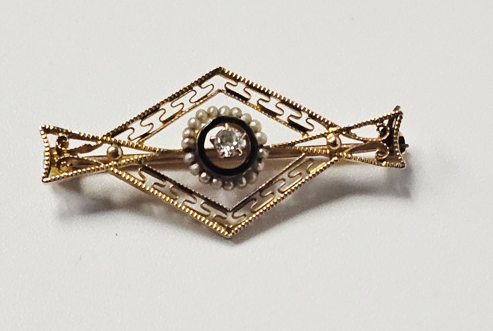 10K & Diamond Art Deco Style Bar Brooch 1.4 Grams: This Art Deco style filigree bar brooch is constructed from 10k yellow gold. The piece features a central rhombus-shaped frame decorated with a repeating Greek key or meander openwork pattern and milg