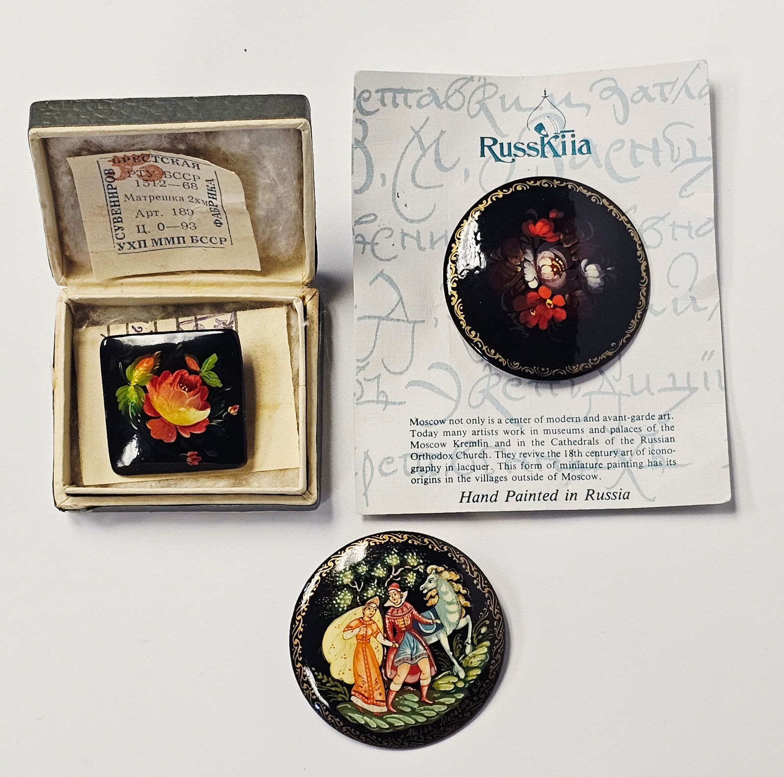 Fedoskino and Soviet Schools, Group of Three Lacquer Brooches, Papier-mache and Paint, circa: This lot features three hand-painted Russian lacquer brooches from the Soviet period. The first is a round brooch featuring a polychrome floral bouquet in the Zhostovo style on a black ground with a g