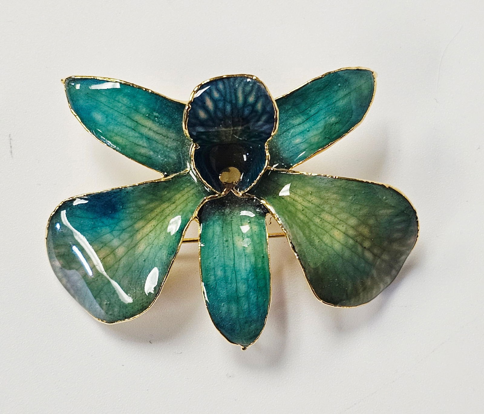 Gold-Plated Natural Orchid Flower Brooch and Pendant: This vintage botanical accessory features a genuine natural orchid flower preserved in a translucent, high-gloss lacquer. The petals display a vibrant gradient of teal, forest green, and deep blue, wi