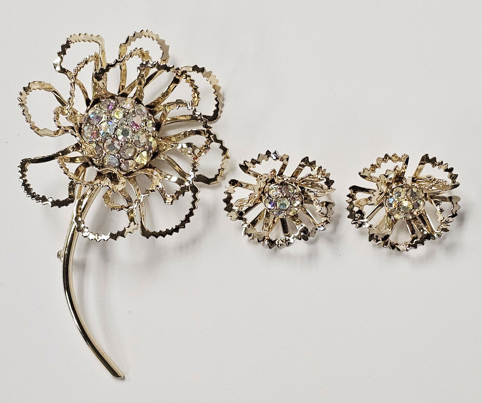 Gold-Tone Sarah Coventry Floral Brooch and Earrings: This vintage costume jewelry set by Sarah Coventry, identified as the Allusion pattern from circa 1968, consists of a large floral brooch and a coordinating pair of clip-on earrings. The pieces are co