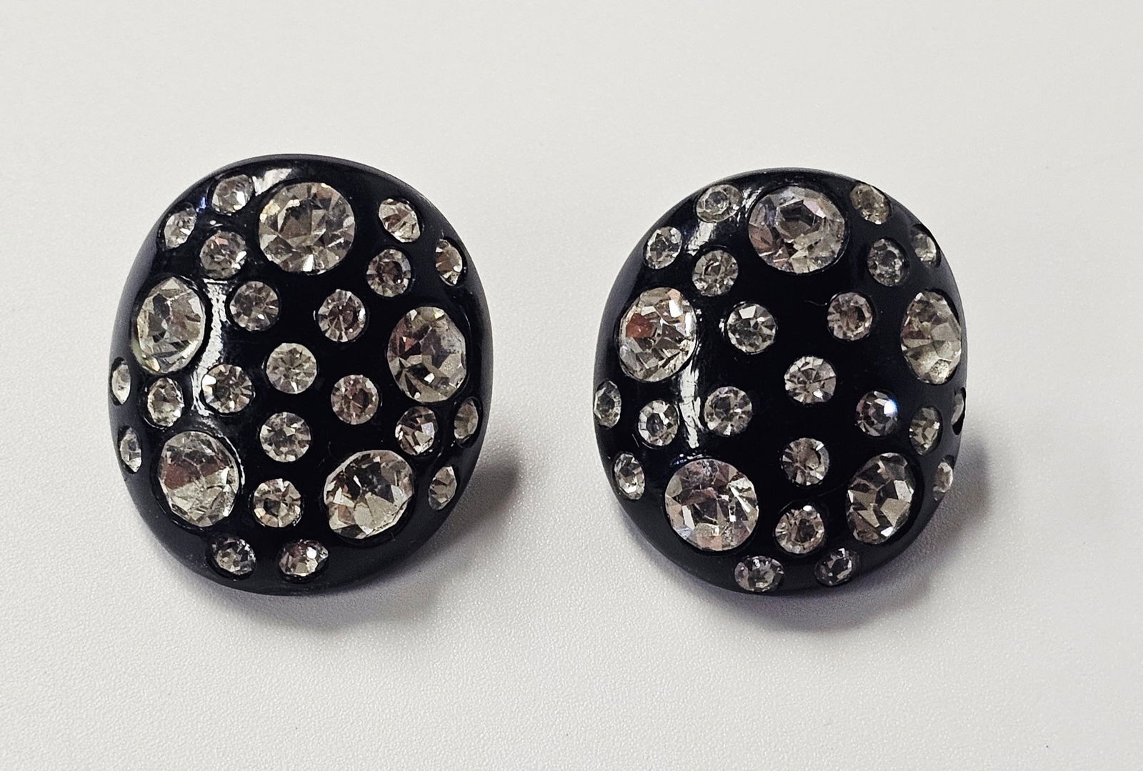 Signed Weiss Black Thermoset & Rhinestones Earrings: This is a matched pair of vintage mid-century costume jewelry earrings by Weiss. The oval, domed earrings are crafted from black thermoset and feature a scattered starburst pattern of clear, round-cut