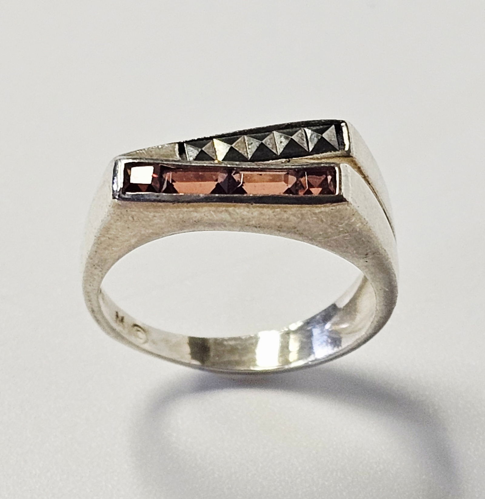 Sterling Silver Garnet and Marcasite Ring 3.4 Grams: This ring is crafted in sterling silver and features a modern bypass-style geometric head. The design is accented by four channel-set, reddish-brown baguette-cut gemstones that appear to be garnets, p