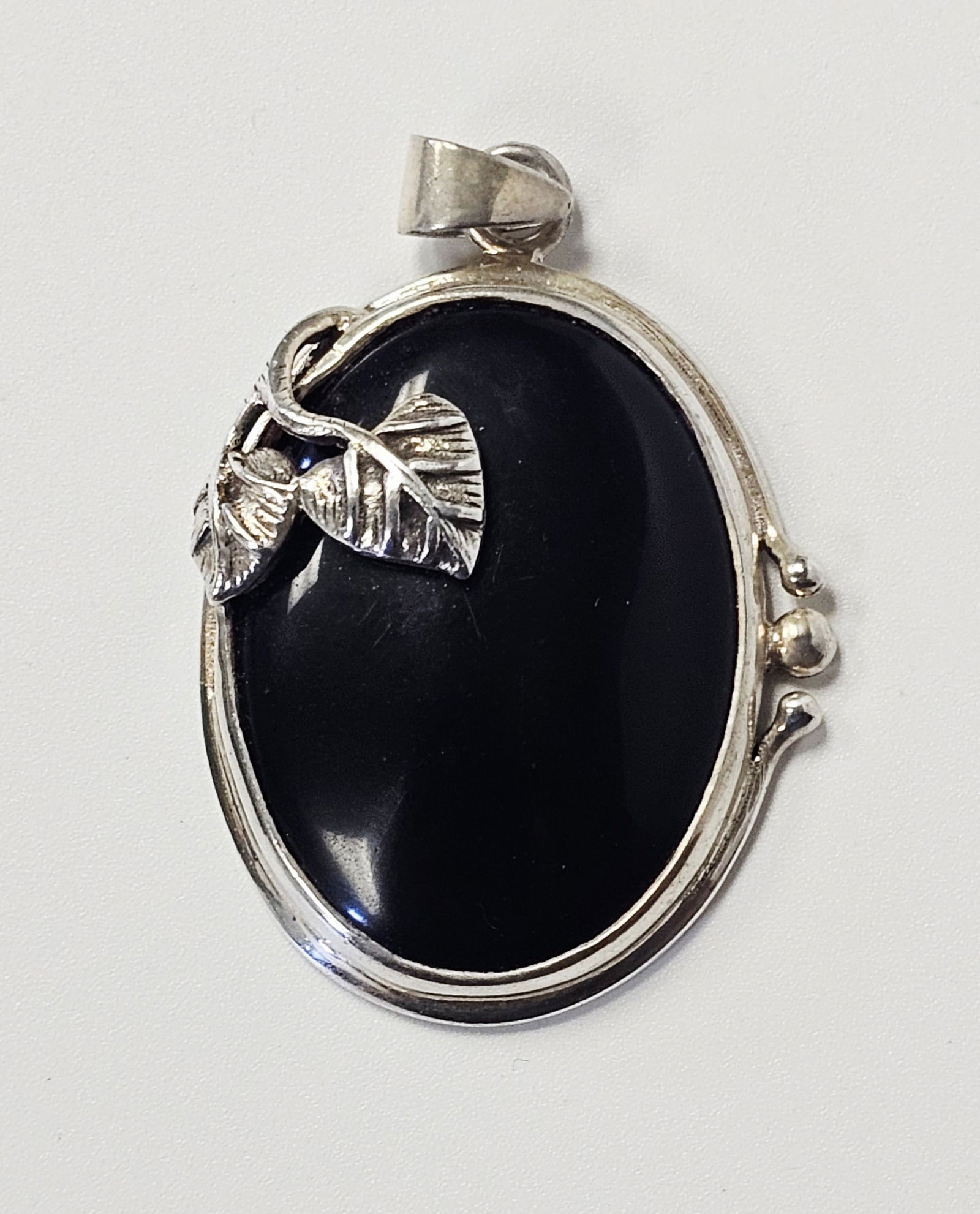 Sterling Pendant with Large Black Cabochon 24 Grams: This pendant is constructed of sterling silver and centers a large, oval, black cabochon-cut gemstone that appears to be onyx. The stone is bezel-set within a polished silver frame. The piece features