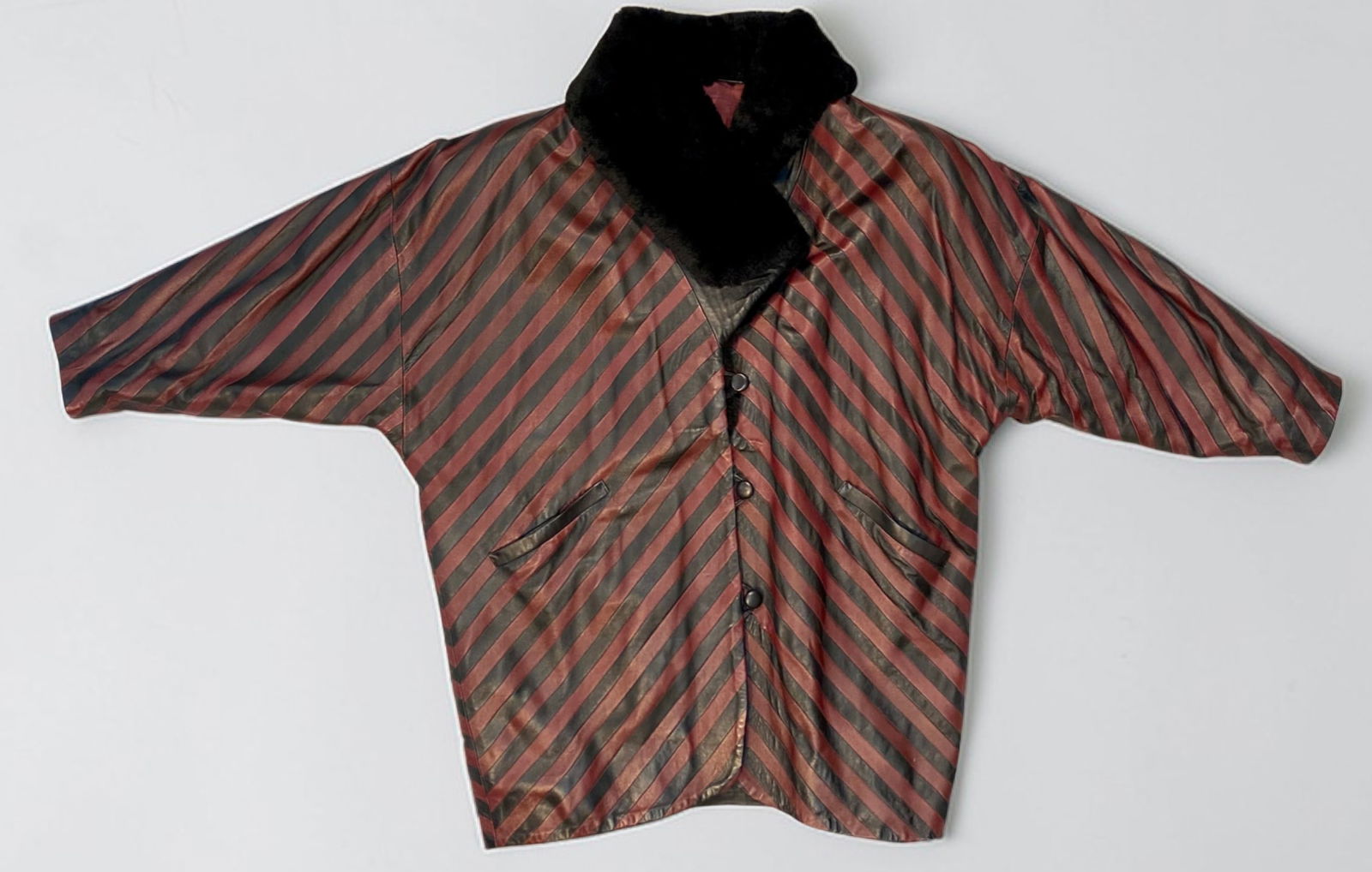 A Vintage Gina Sullivan Striped Leather Jacket with Faux-Fur Collar: A vintage oversized jacket by Gina Sullivan. The garment is constructed from alternating diagonal strips of black and burgundy leather. It features a black faux-fur collar and dolman sleeves. The fron