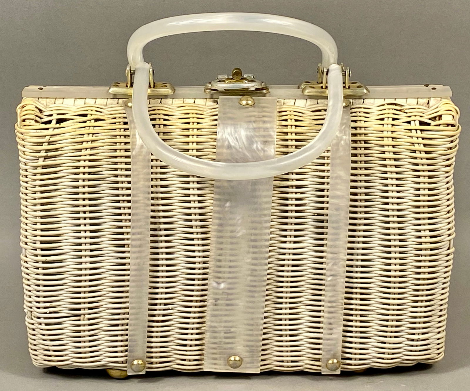 Tropic Imports Vintage Mid-Century Wicker Handbag with Pearlized Lucite Trim: Attributed to Tropic Imports, this mid-century box-style handbag features a cream-colored woven rattan body. The structured design is accented with pearlized white Lucite top trim, three decorative ve