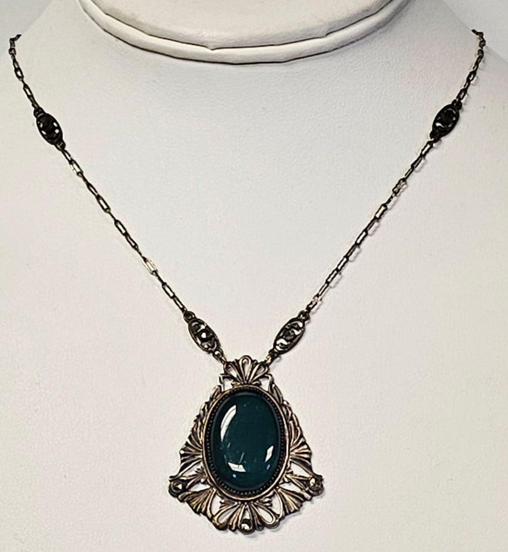 Silver-Toned Necklace with Green Cabochon and Metallic Accents: A silver-toned necklace featuring an ornate pendant set with a large oval dark green cabochon stone and small faceted metallic accents, with the pendant measuring approximately 20 inches in length. Fa