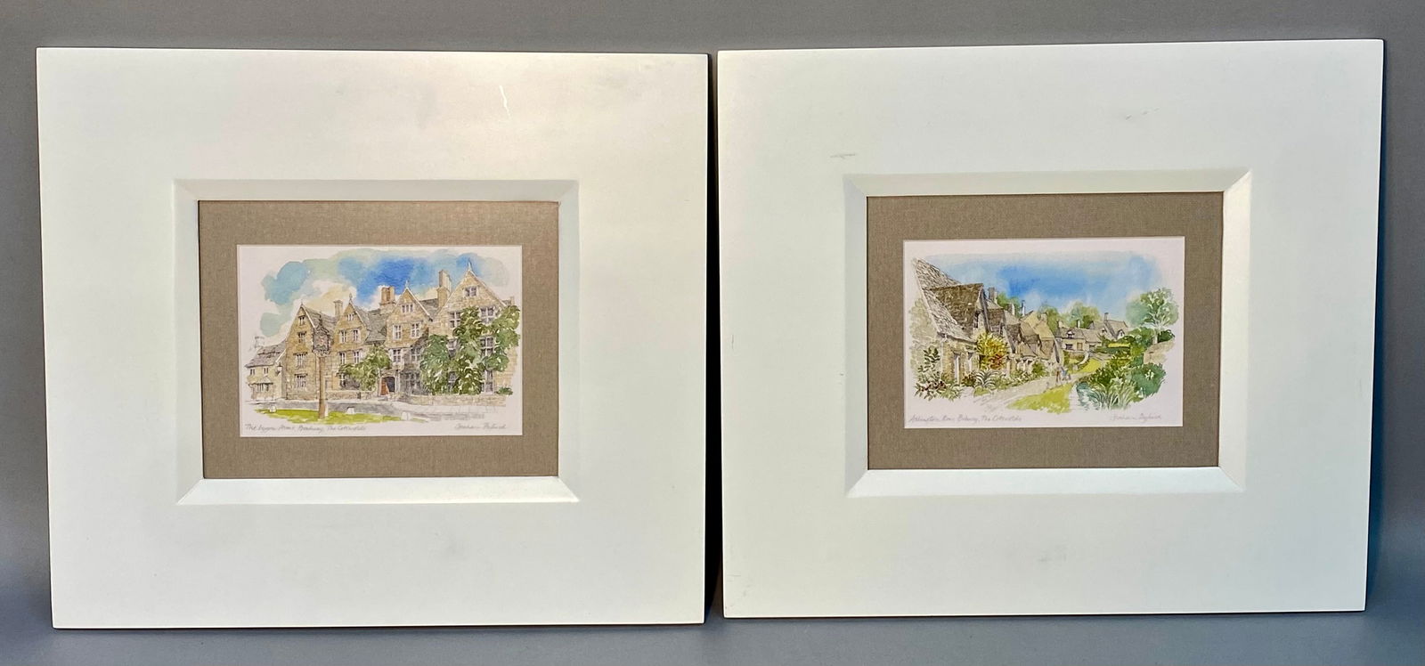 A Pair of Graham Byfield Cotswolds Illustrated Framed Prints: This pair of framed prints is from the Cotswolds Illustrated series by English artist Graham Byfield. The representational landscapes depict The Lygon Arms, Broadway and Arlington Row, Bibury. These p