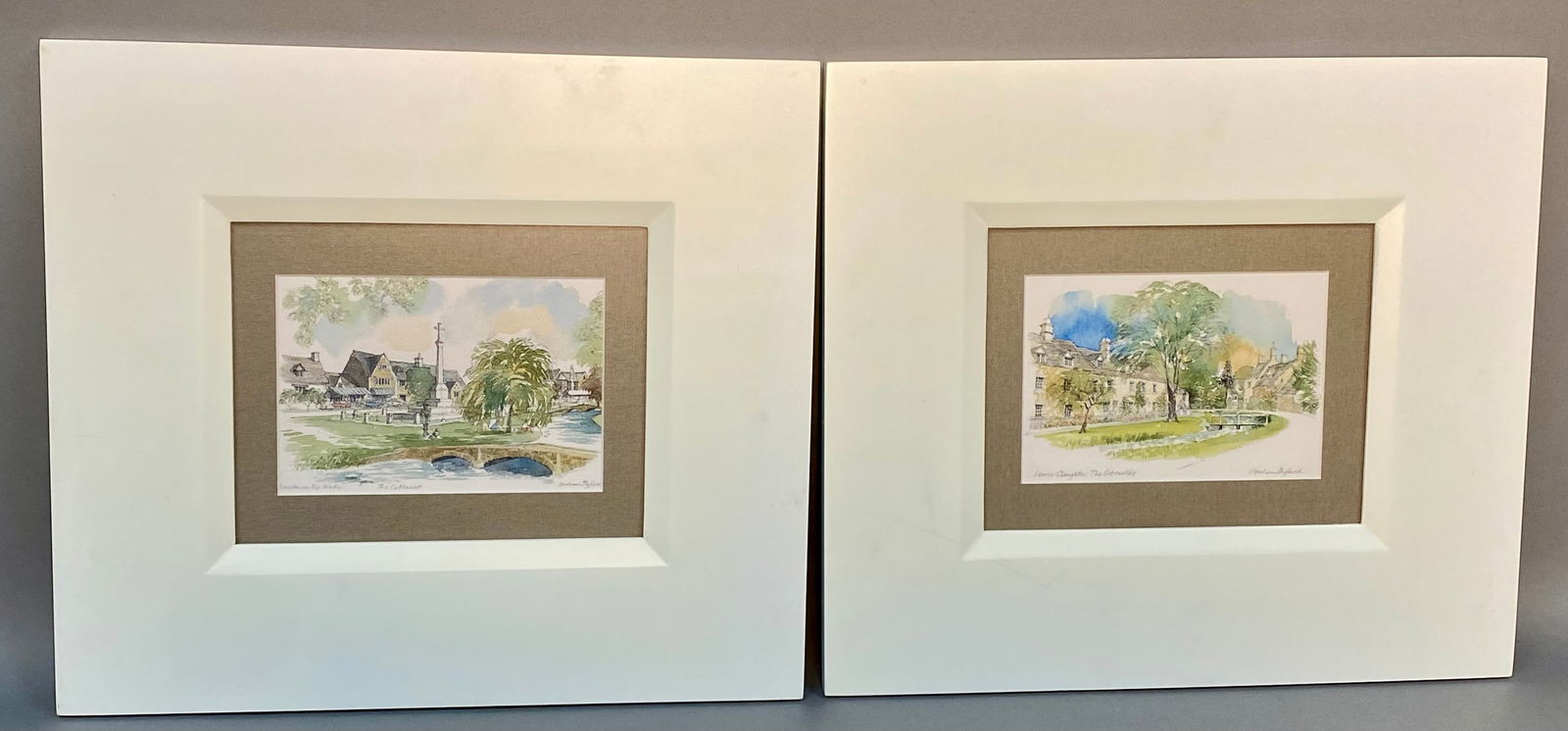 A Pair of Graham Byfield Cotswolds Art Prints: A pair of framed prints after original watercolors by Graham Byfield, depicting village scenes in the Cotswolds, England. The scenes are titled Bourton-on-the-Water and Lower Slaughter. Each print is