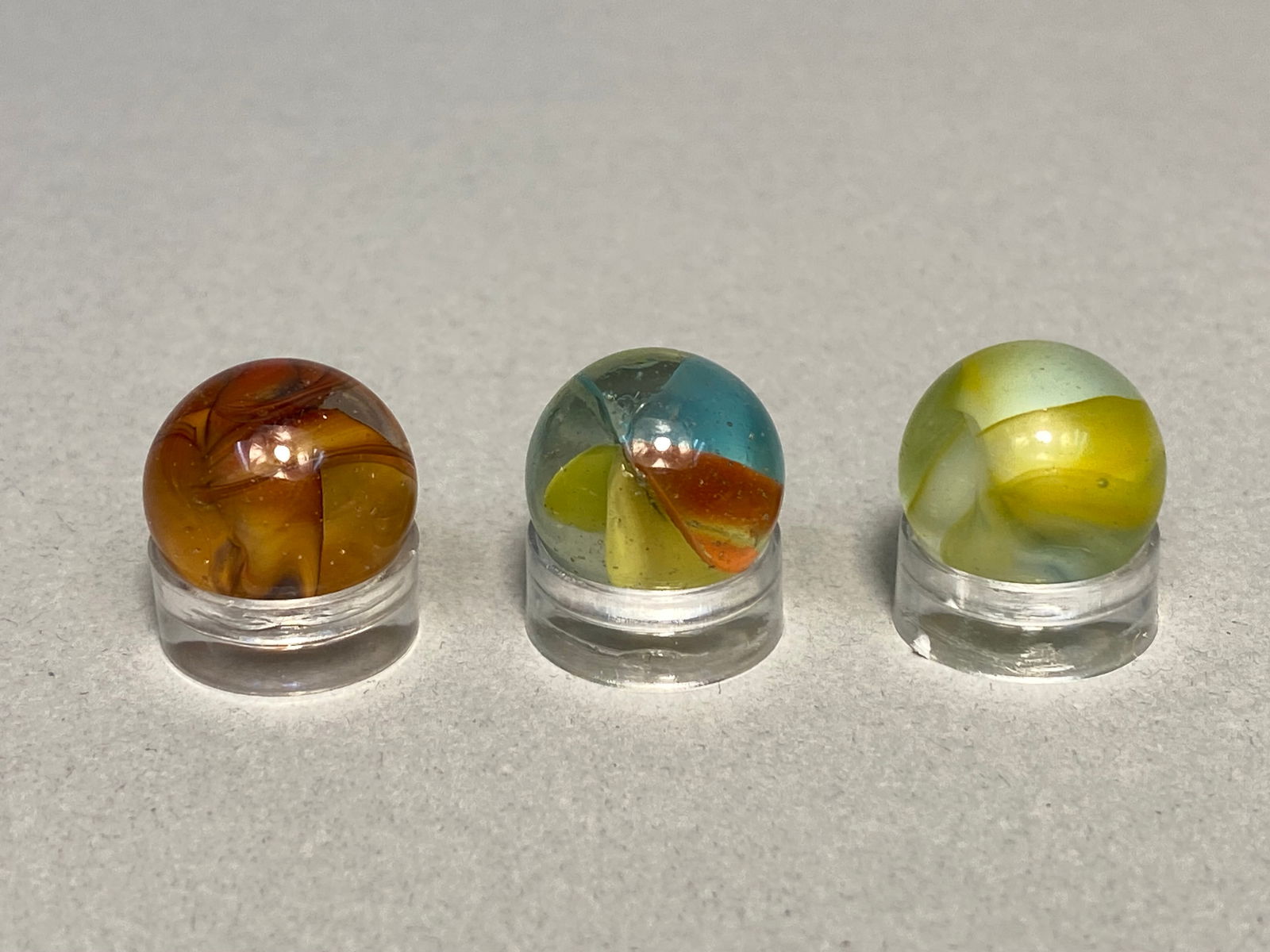 Three Vintage Tri-Color Cat's Eye and Swirl Glass Marbles, circa 1950s: This lot features three vintage machine-made glass marbles, showcasing popular mid-century designs. The collection includes one tri-color hybrid cat's eye marble, which contains internal vanes of blue