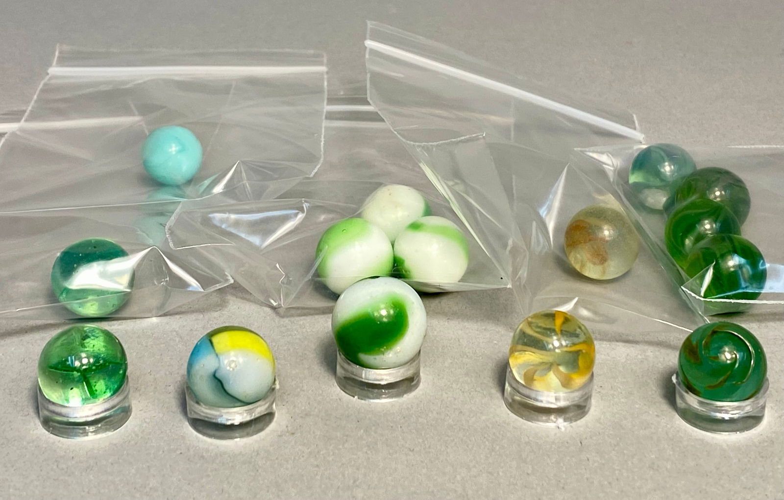 Akro Agate and Assorted Makers, Vintage Glass Marble Collection, Greenies and Multi-Color Swirls,: This collection features a diverse assortment of 15 machine-made glass marbles, primarily attributed to the Akro Agate Company and other mid-century American manufacturers. The lot includes several cl