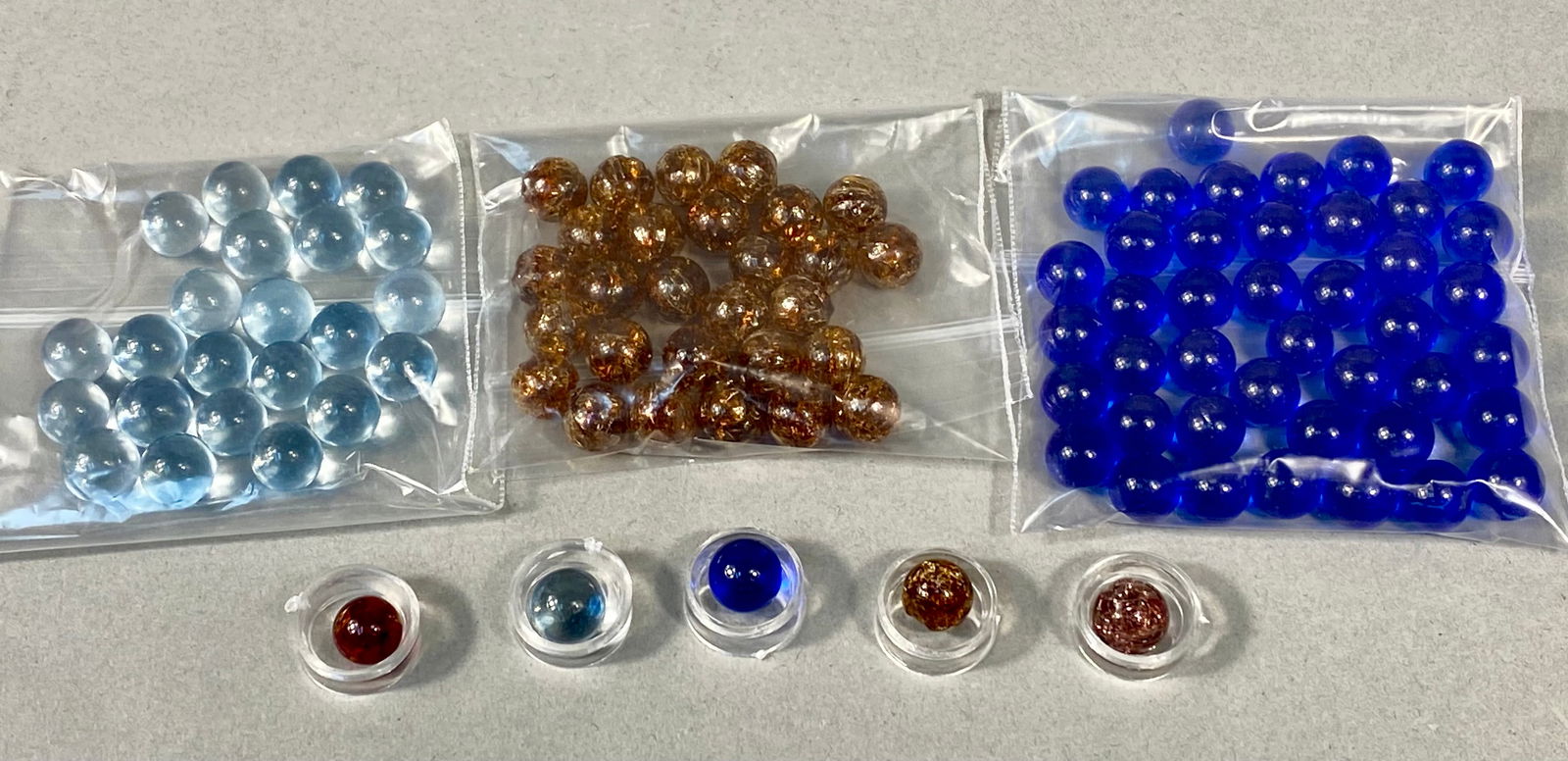 A Collection of Assorted Glass Marbles: A collection of glass marbles. The assortment includes specimens in translucent light blue, cobalt blue, and red, as well as amber and pinkish-mauve examples characterized by a crackled or fried inter