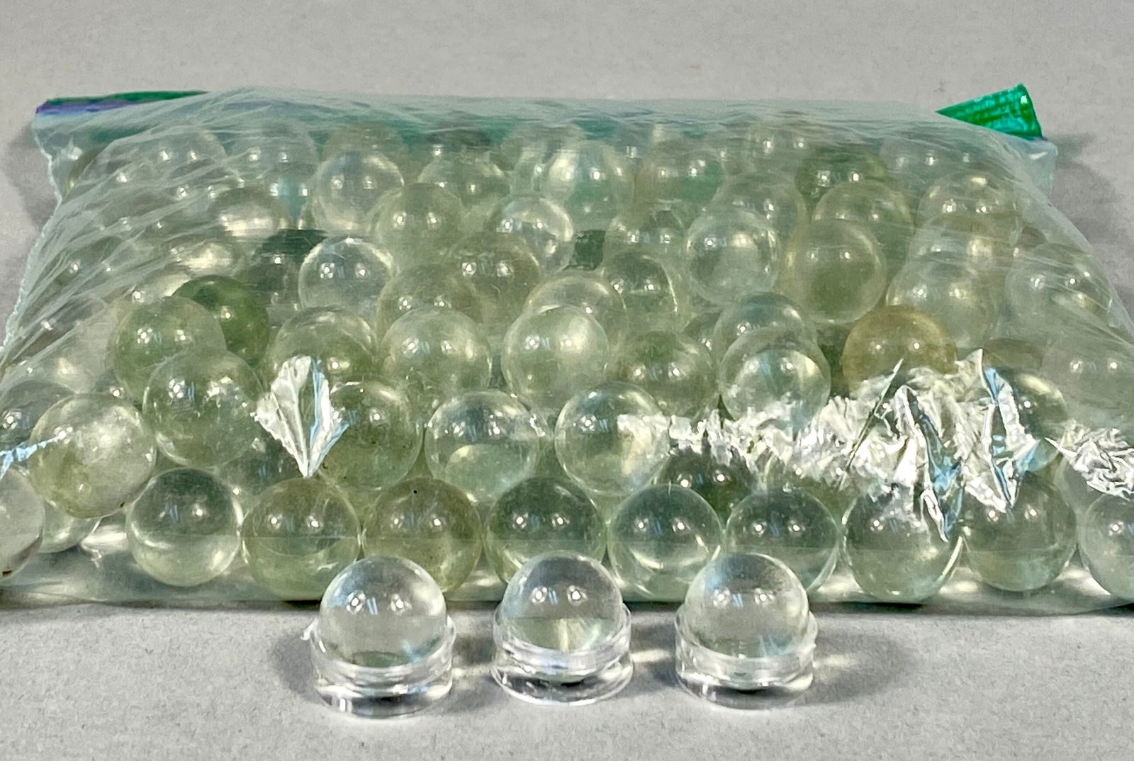 Unmarked Bulk Collection of Clear Glass Marbles, Approximately 9/16 Inch, Late 20th to Early 21st: This lot consists of a bulk collection of several dozen machine-made clear glass marbles. The spheres are crafted from transparent glass, with select pieces exhibiting subtle greenish or yellow-amber