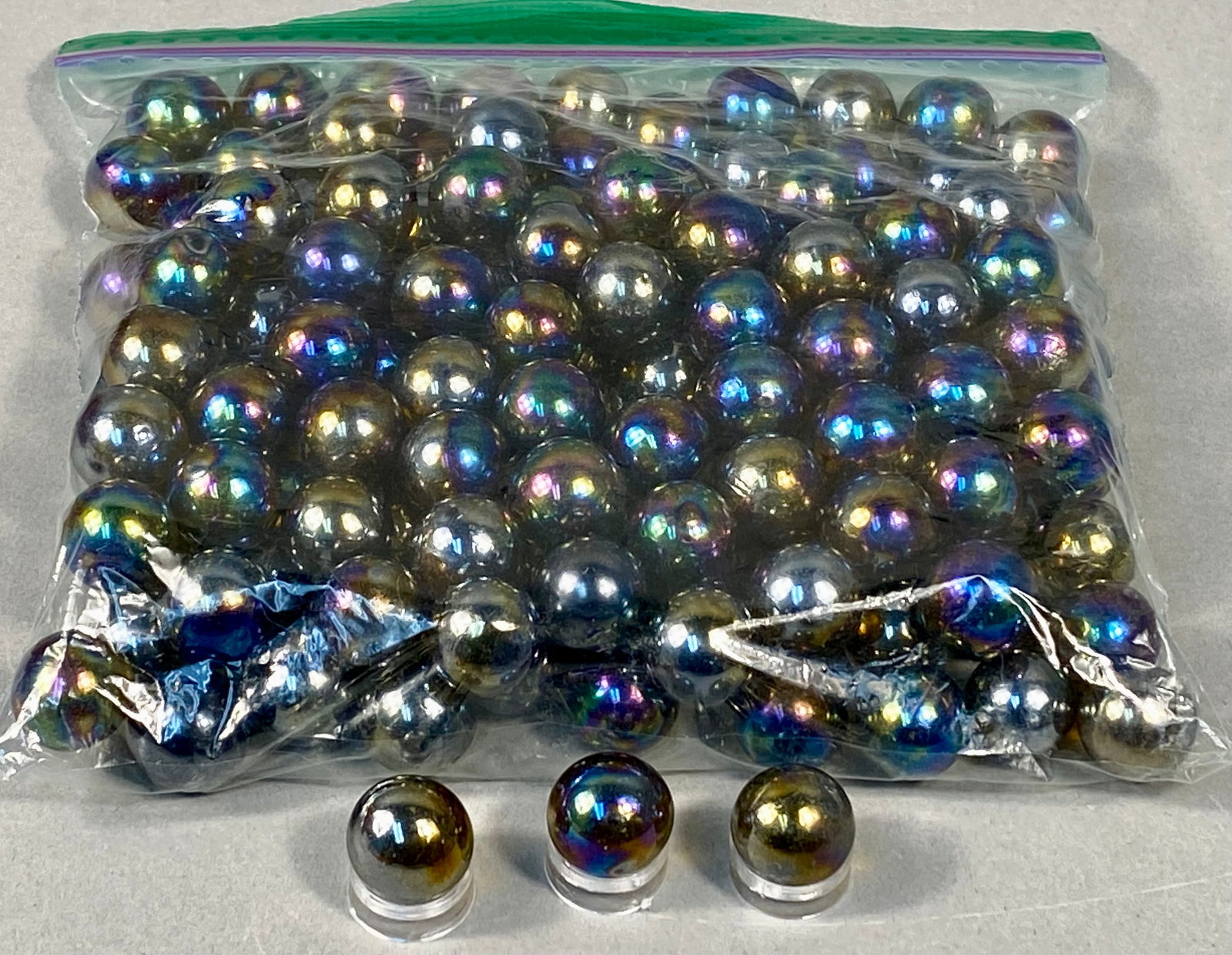 Mega Marbles Meteor Iridescent Glass Player Marbles, Late 20th Century: This collection features a large assortment of machine-made glass player marbles from the Mega Marbles Meteor line. Each sphere is finished with a distinctive metallic iridescent coating, often referr