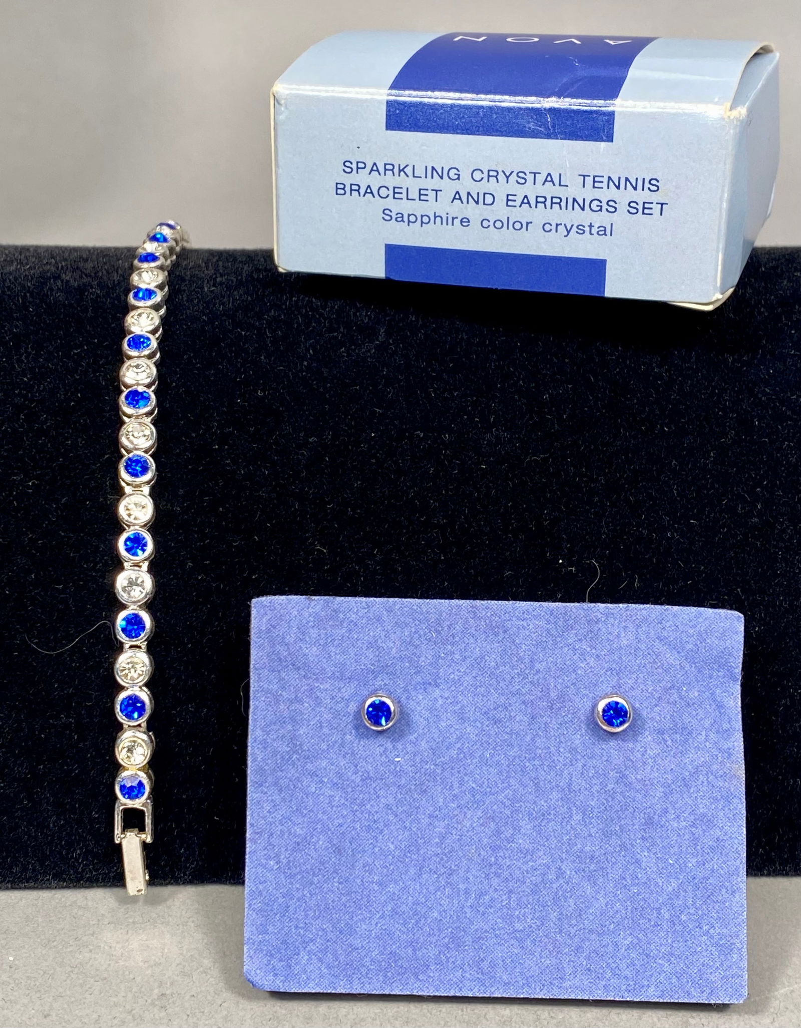 Silver-Tone Sapphire-Colored and Clear Crystal Jewelry Set, Avon: This costume jewelry set by Avon consists of a tennis-style bracelet and a coordinating pair of stud earrings. The set is crafted from silver-tone base metal. The bracelet features a continuous line o