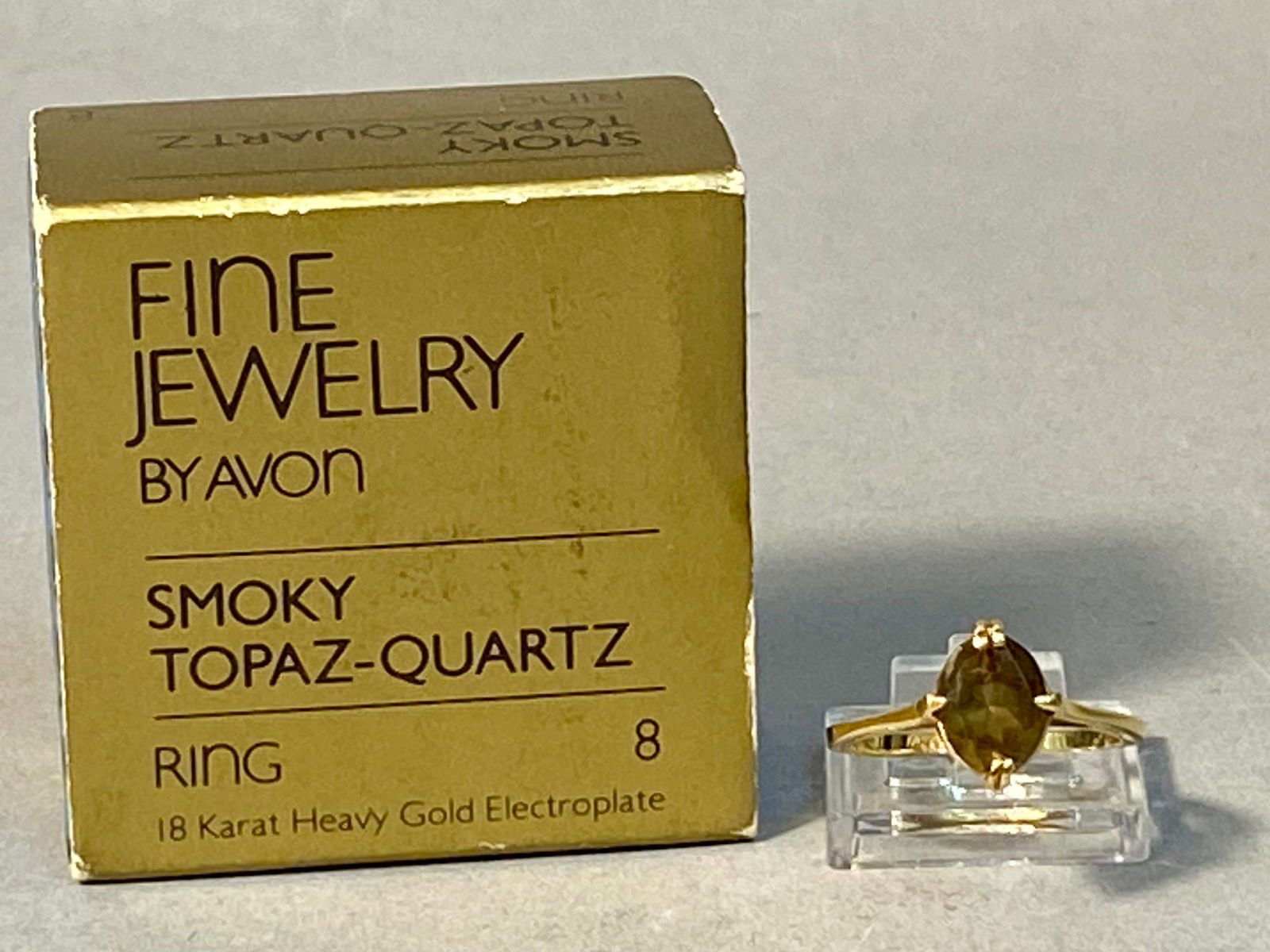 18K Heavy Gold Electroplate Solitaire Ring with Smoky Topaz-Quartz: This is an 18 karat heavy gold electroplated solitaire cocktail ring manufactured by Avon. The ring features a centrally mounted oval-cut smoky topaz-quartz gemstone characterized by a translucent bro
