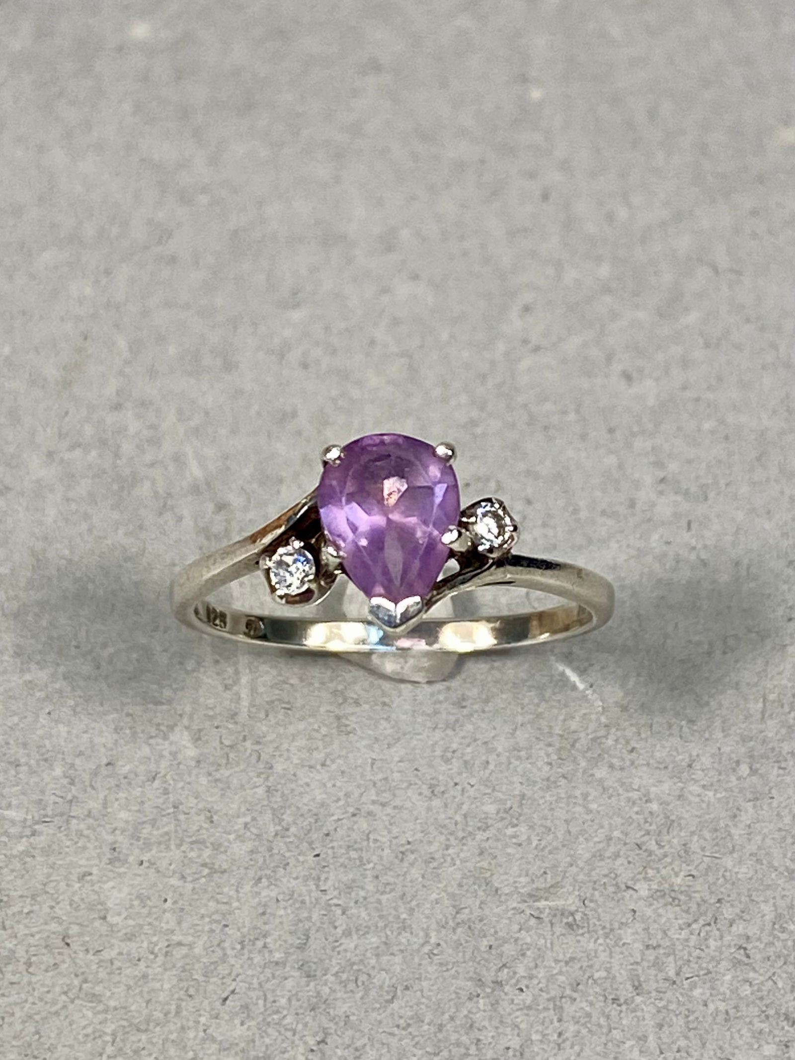 Sterling Silver Pear-Cut Amethyst and Colorless Accent Stone Ring, 2.3g: This ring is crafted in sterling silver and features a central pear-cut purple gemstone that appears to be an amethyst. The center stone is secured by a four-prong setting with a protective V-tip at t
