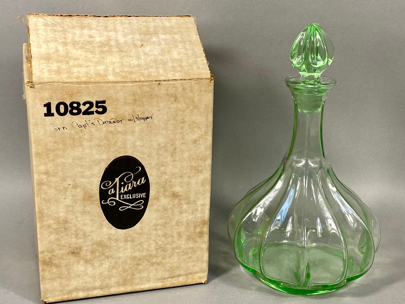 Tiara Exclusive Green Pressed Glass Captain's Decanter: A vintage Tiara Exclusive decanter in the Captain's pattern, crafted from transparent light green pressed glass. The vessel features a bulbous, multi-ribbed body that tapers into a slender neck with a
