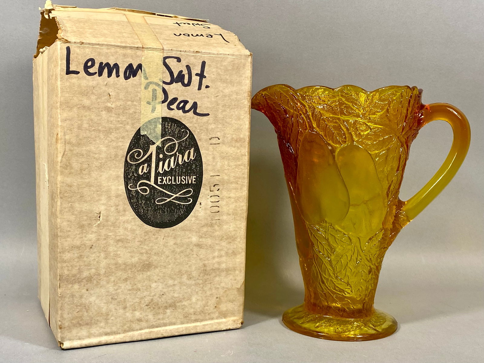 Tiara Exclusive Pressed Glass Sweet Pear Pattern Pitcher: Produced by Indiana Glass for Tiara Exclusive, this vintage pitcher is executed in the "Sweet Pear" pattern. The piece is crafted from translucent amber-yellow pressed glass, identified as &