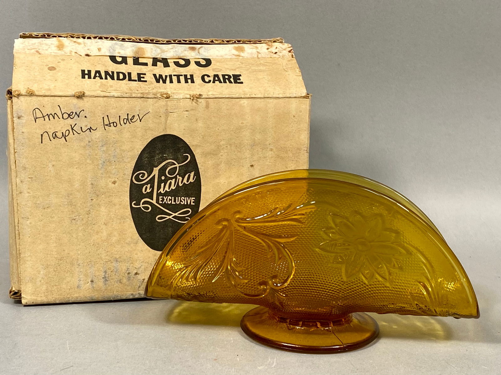 Tiara Exclusive Sandwich Pattern Amber Glass Napkin Holder: This vintage napkin holder is a classic example of mid-to-late 20th-century pressed glass. Produced by the Indiana Glass Company for Tiara Exclusive, the piece is rendered in a deep amber color. It fe