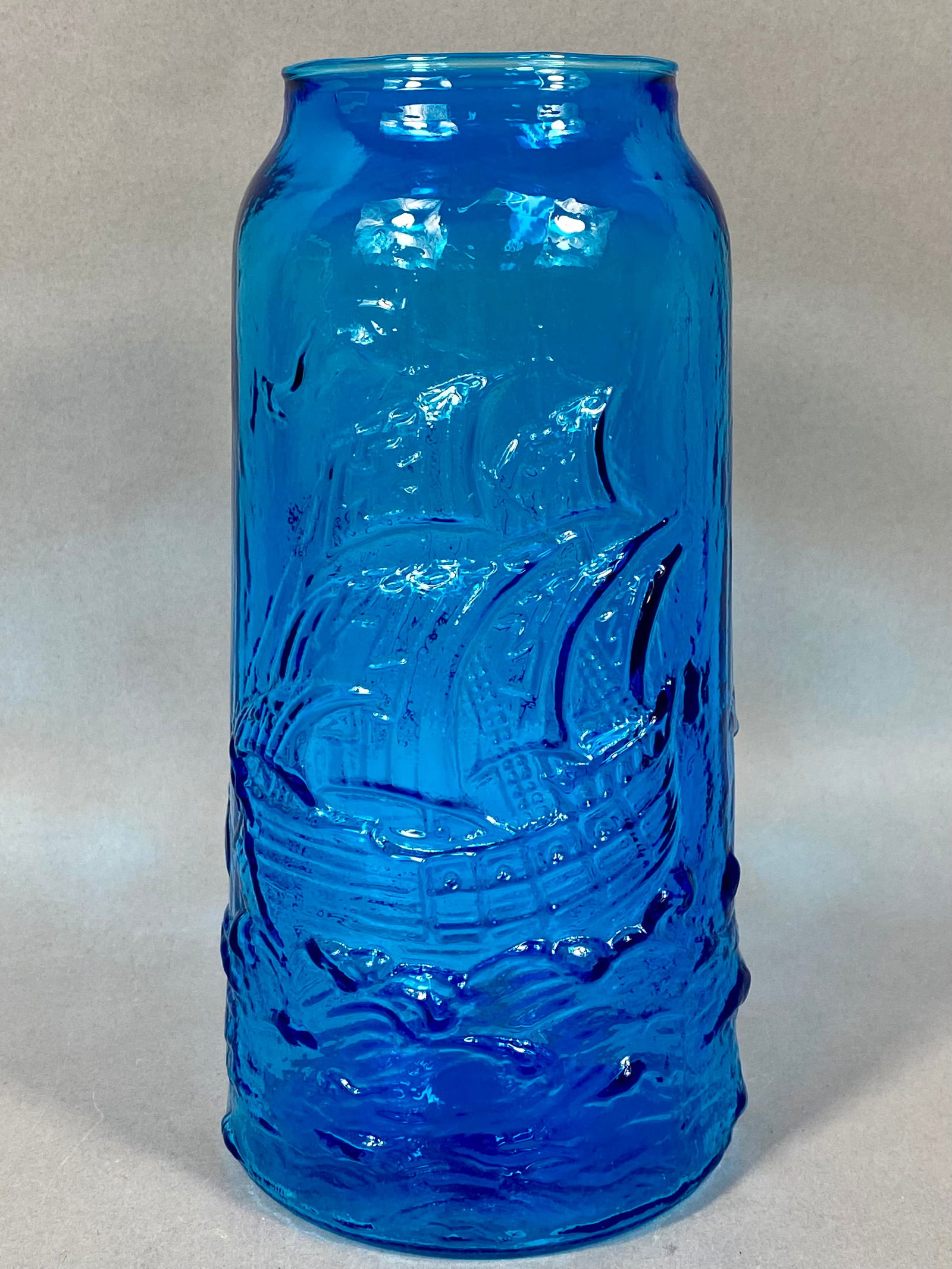 Mid-Century Modern Molded Glass Nautical Motif Vase: This mid-century modern art glass vase is rendered in a translucent aqua blue color. The exterior is finished with a high-relief molded design over a textured bark-like ground. The decorative program