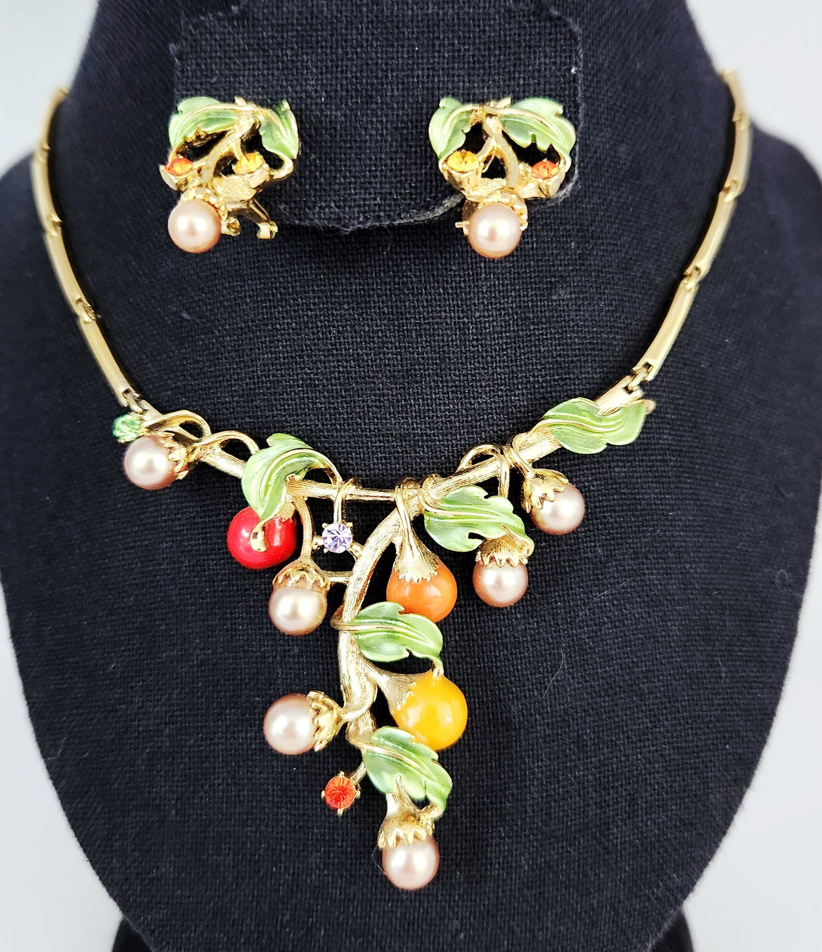 Vintage Gold-Tone Botanical Necklace & Earrings Set: This vintage costume jewelry set includes a necklace and a pair of matching earrings featuring a botanical motif. The pieces are crafted from gold-tone metal and decorated with green enameled leaves a