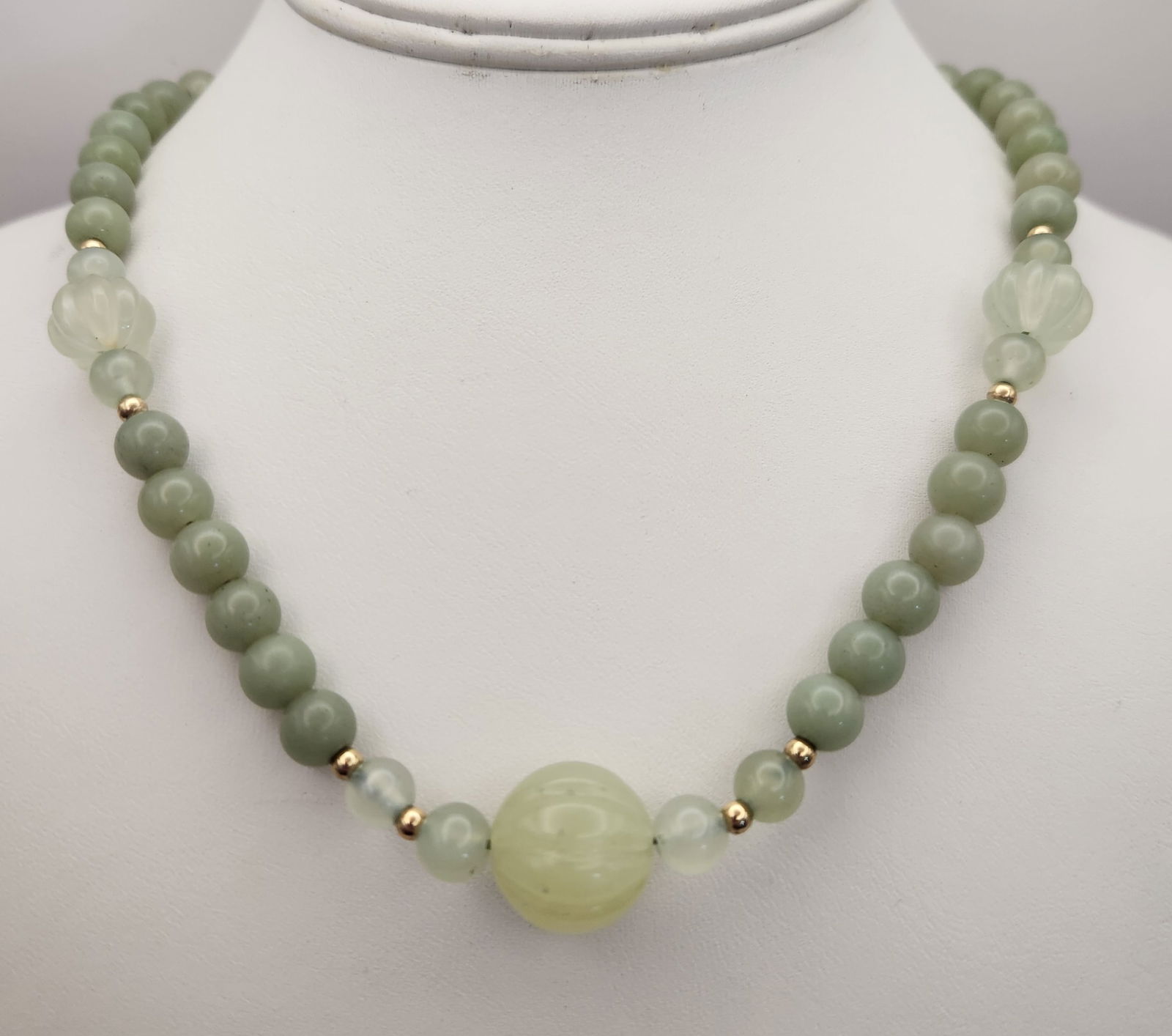 Graduated Jadeite Bead Necklace With Carved Accents: A single-strand necklace featuring a collection of light to medium green stone beads in both spherical and carved fluted forms. The beads are arranged in a graduated fashion, with the largest carved b