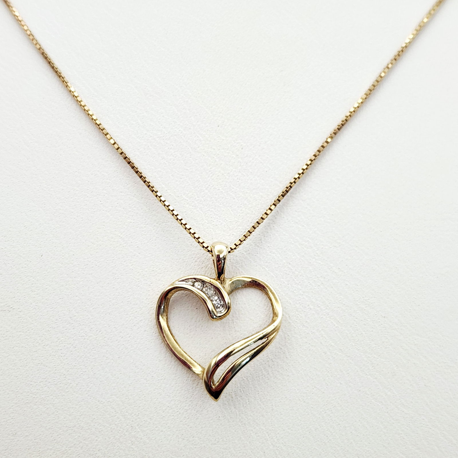 10K Gold Clear Stone Heart Necklace 2.2 Grams: A 10-karat yellow gold necklace featuring an openwork stylized heart-shaped pendant. The pendant is accented with small round-cut clear stones set within a curved channel. The piece is suspended from