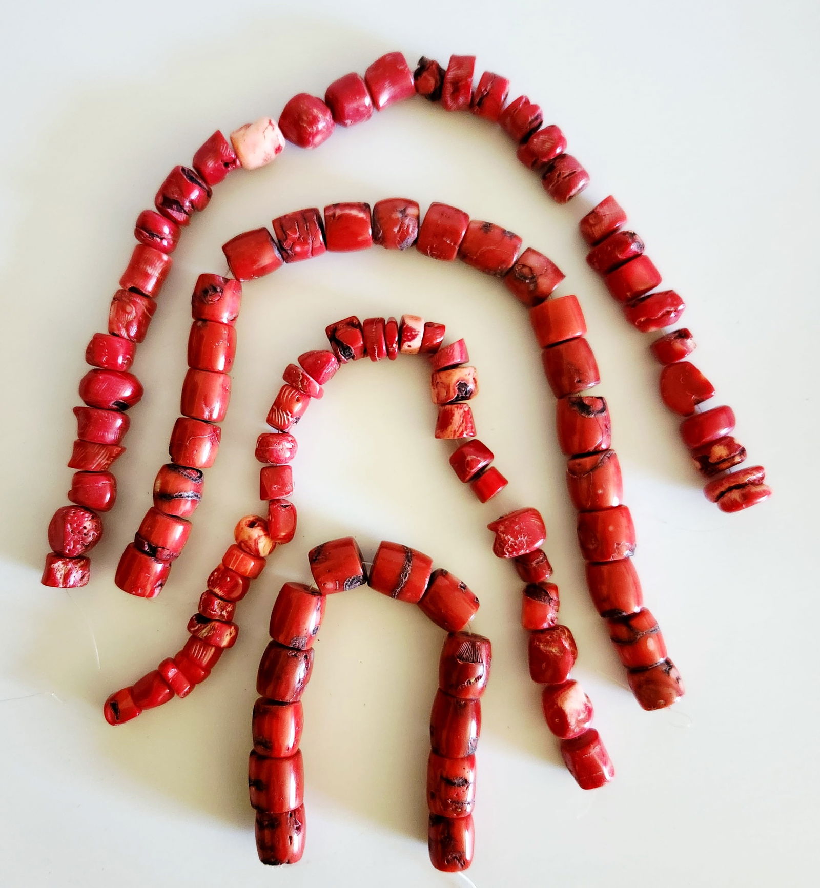 Collection of Red Sponge Coral Beads: A collection of red coral beads, likely sponge or apple coral, featuring a vibrant red hue with natural dark-toned inclusions, pitting, and striations characteristic of the material. The beads are fas
