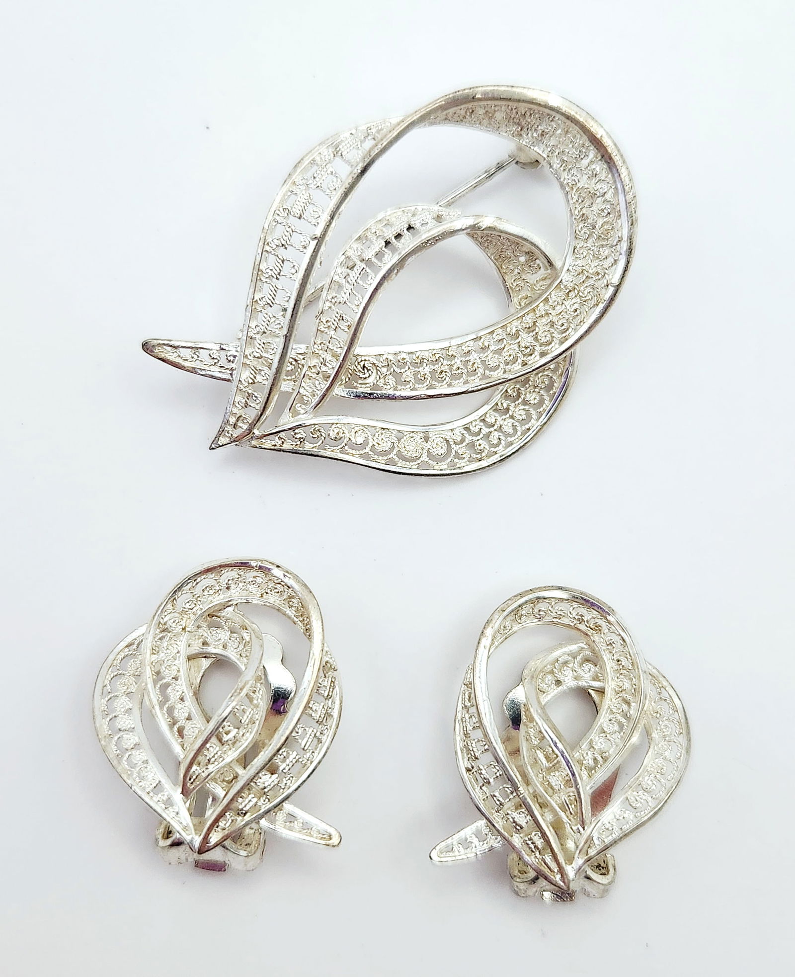 Sterling Silver Filigree Brooch and Clip-on Earring Set, EB Germany: This vintage jewelry suite comprises a brooch and a pair of matching clip-on earrings, characterized by a stylized, swirling foliate design. The pieces are constructed from sterling silver featuring d