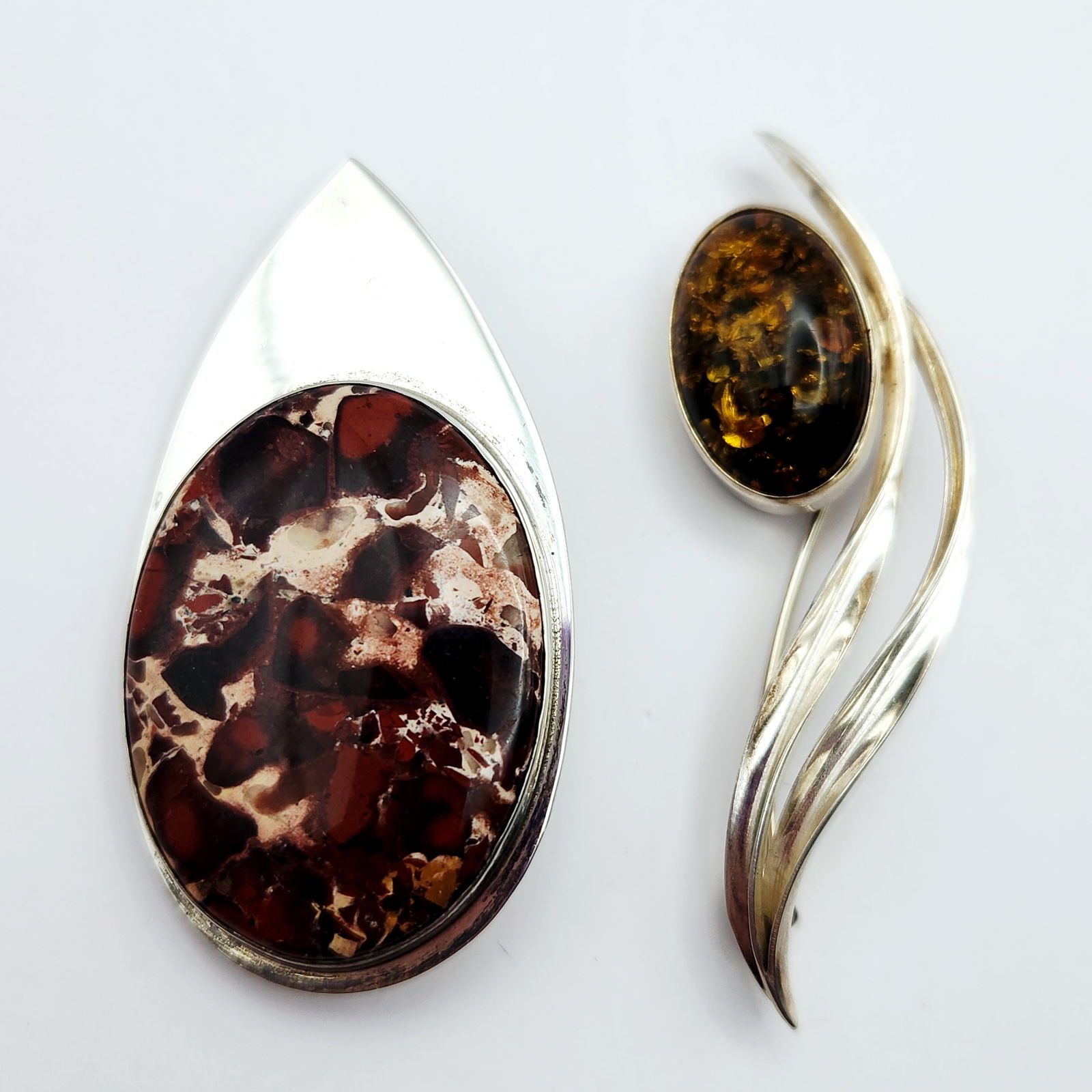 Sterling Modernist Brooches 33.5 Grams: This lot consists of two sterling silver brooches featuring large gemstone cabochons. The first is a modernist, wave-form brooch crafted in sterling silver, bezel-set with an oval cabochon that appear