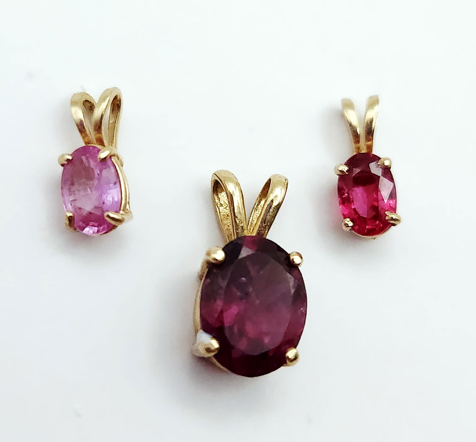 14K Gold Multi-Gemstone Pendants 1.9 Grams: A collection of three 14 karat yellow gold pendants featuring oval faceted gemstones. The group includes one larger pendant set with a deep purplish-red rhodolite garnet measuring approximately 8mm x