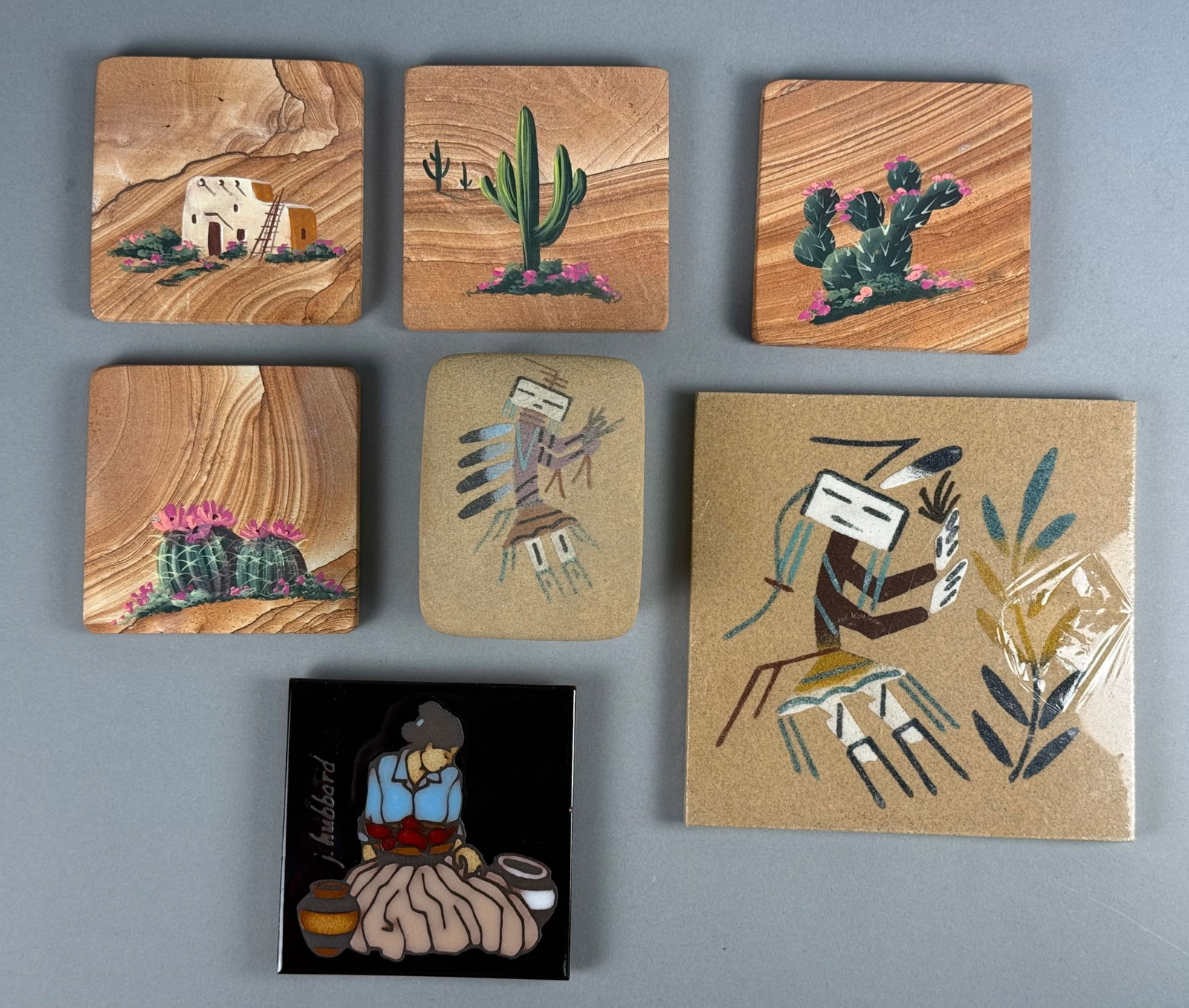 A Collection of Southwest Themed Decorative Items: A collection of Southwest themed decorative items comprising sandstone coasters, sand art tiles, and a ceramic lidded box. The group includes four square sandstone coasters featuring hand painted dese