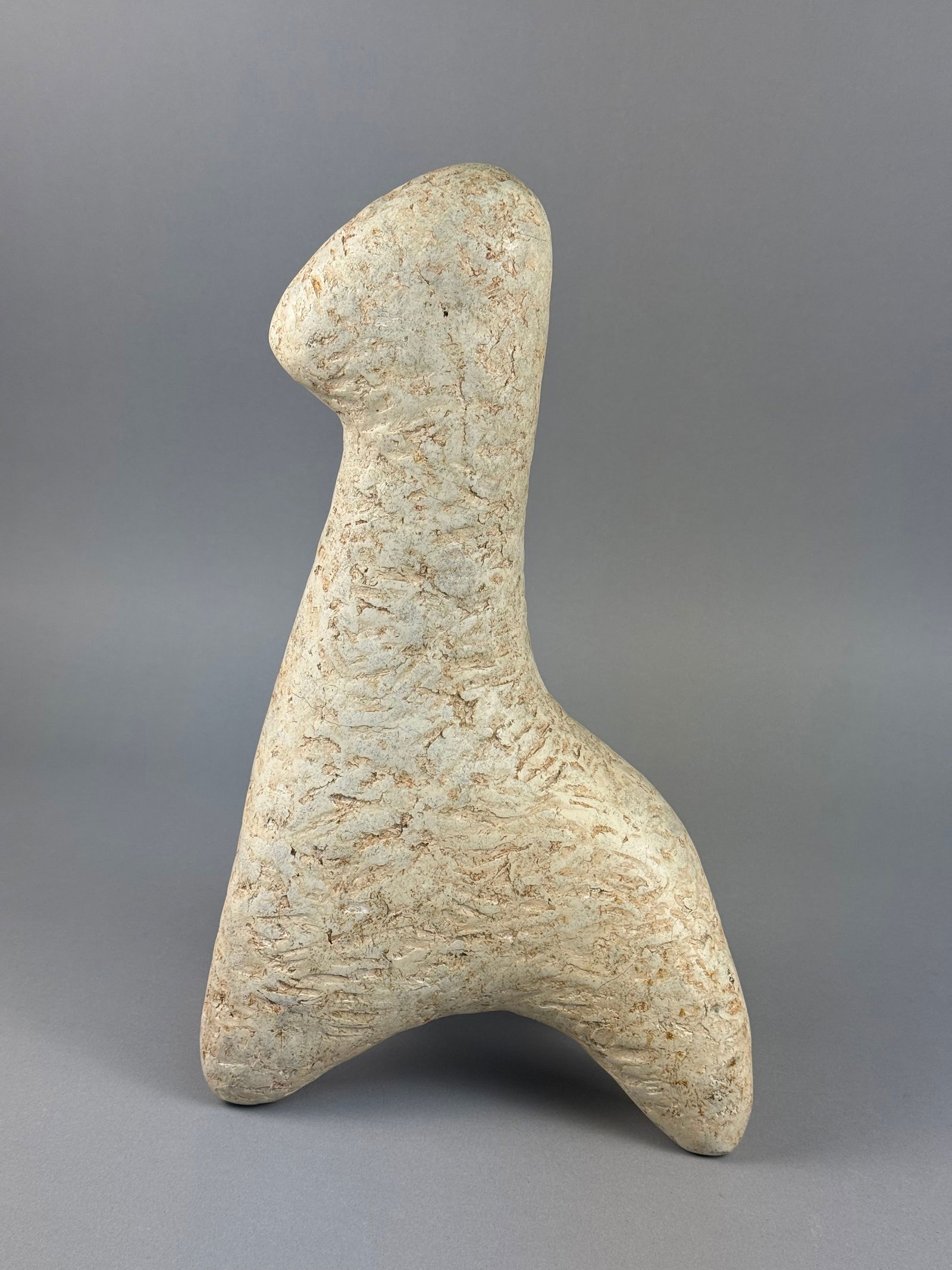 A Modernist Biomorphic Textured Stone Sculpture Signed LYNN: A Modernist biomorphic sculpture crafted from a textured stone or composite material. The object features an elongated body tapering to a rounded end and rests on a tripod-like base. The surface is he
