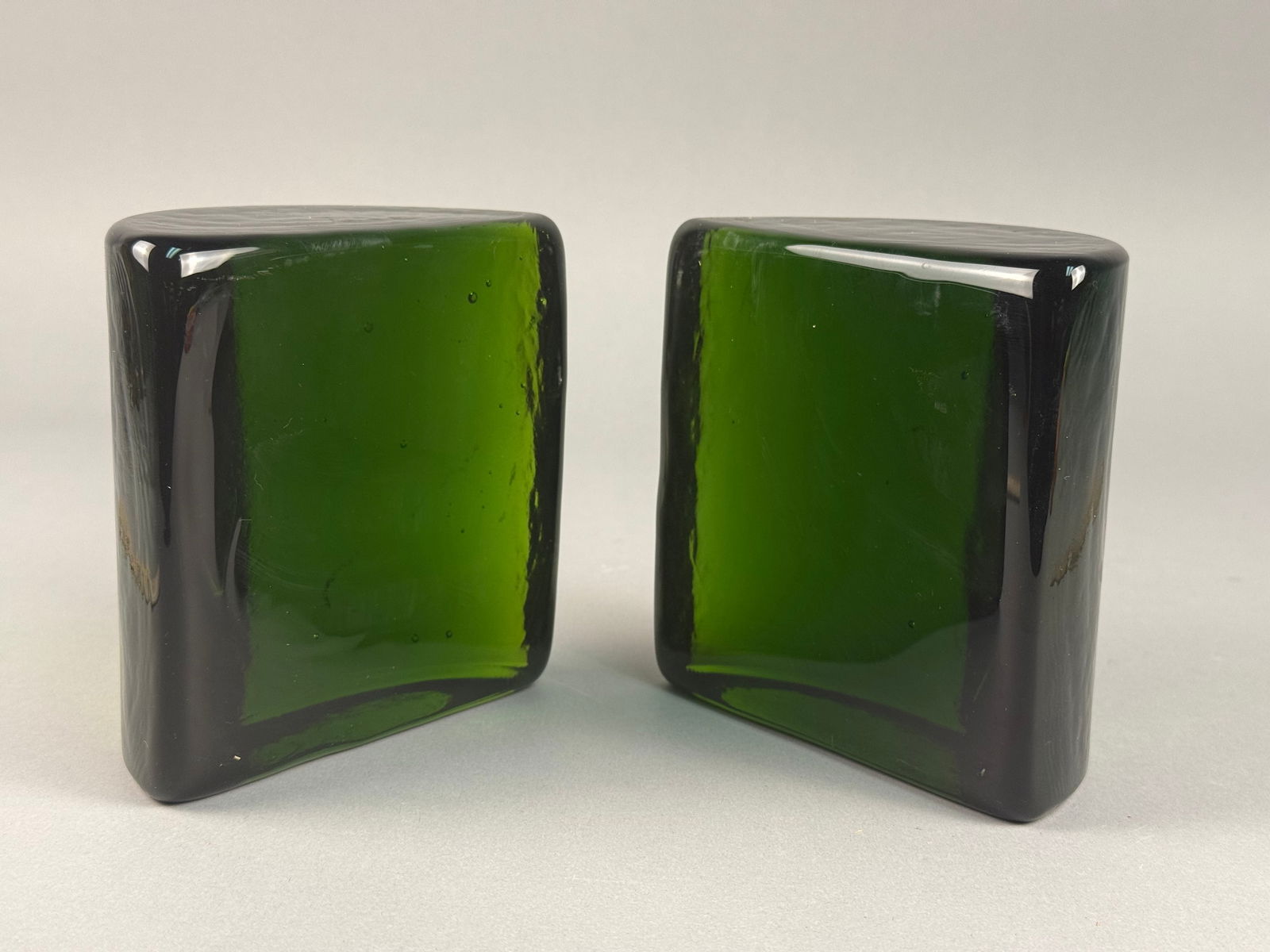 A Pair of Napco Cleveland Emerald Green Glass Bookends, No. 1164: A pair of Napco Cleveland emerald green glass bookends, model number 1164. These solid glass objects are rendered in a minimalist mid-century modern style. Each piece is formed in a semi-circular, D-s