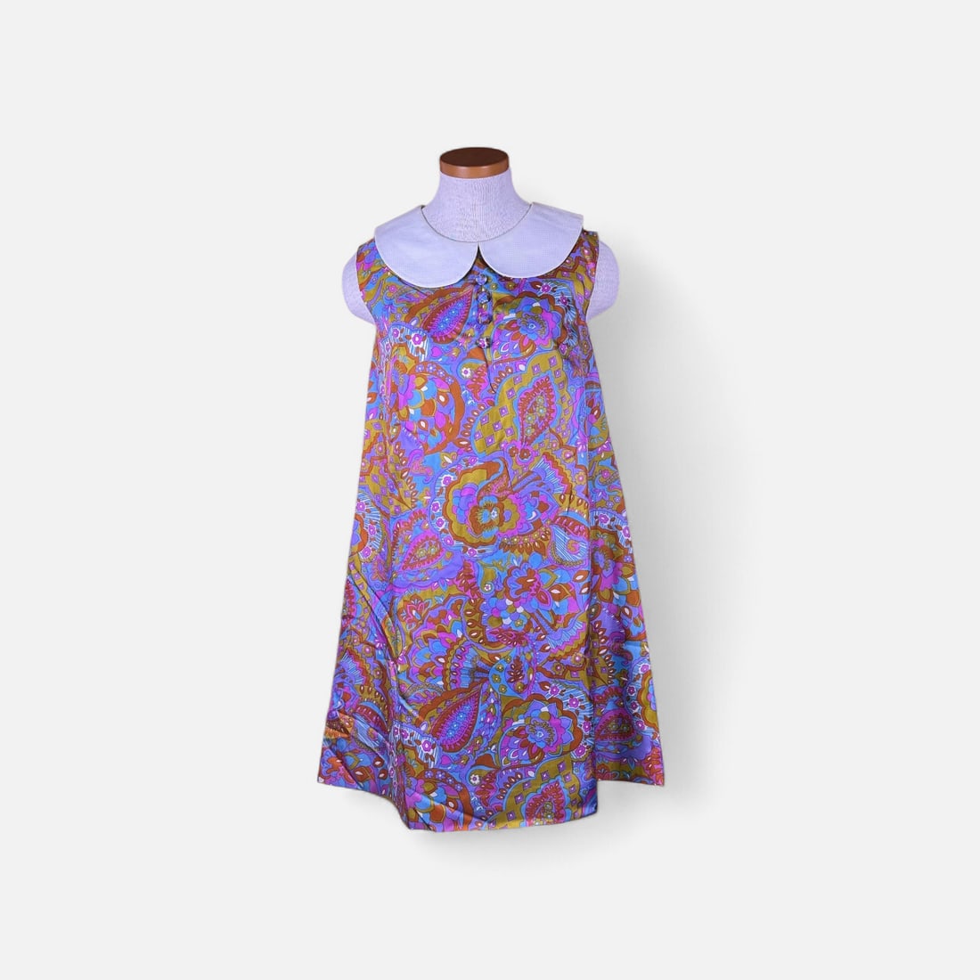 Vintage 1960s Psychedelic Paisley Print A-Line Dress with Peter Pan Collar: A vintage 1960s sleeveless A-line dress featuring a vibrant, multicolored psychedelic paisley and floral print in shades of blue, magenta, purple, and olive. The garment is constructed from a lustrous