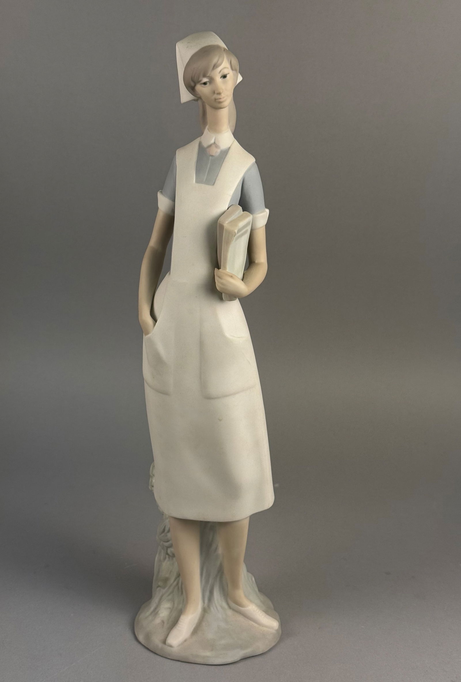 Lladro 4603 Nurse Porcelain Figurine: A Lladro porcelain figurine titled Nurse, model number 4603. This hand-painted sculpture is executed in a matte gres finish featuring a palette of muted blue, white, and gray tones. The figure is